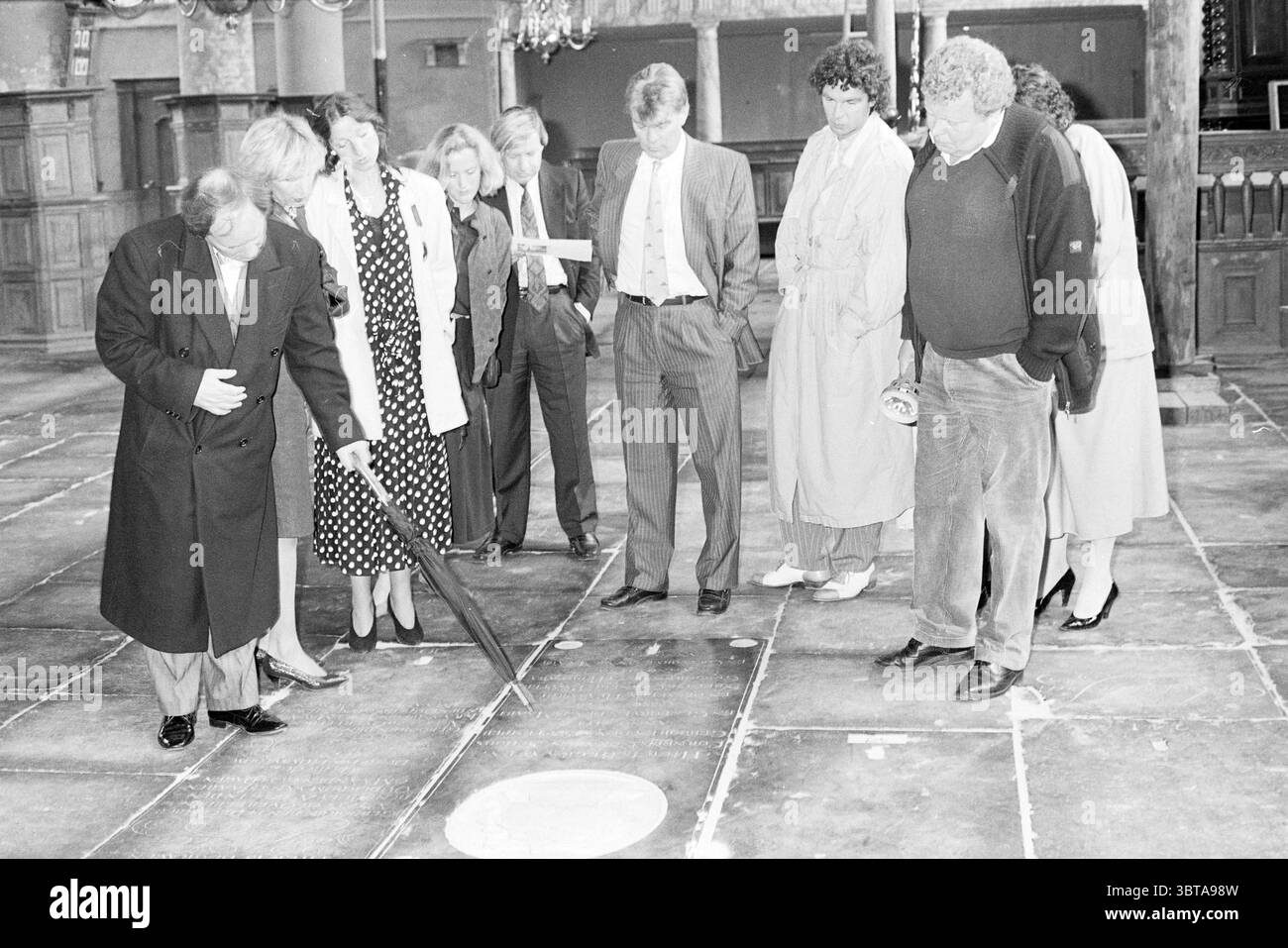 Entreprise Holleman rénovation église Broek in Waterland Churches rénovation Broek in Waterland, Whizgle News, Dutch Desk, pays-Bas, 1950 - 2000 on 05-06-1987. L'image contient ces rubriques. Dans un cadre intérieur historique, un groupe d'individus est rassemblé, apparemment engagé dans l'observation étroite du sol sous eux. L'environnement présente des poutres en bois rustiques et une toile de fond architecturale ornée, suggérant un lieu avec une histoire riche et de caractère. Le groupe se compose d'hommes et de femmes habillés dans un mélange de vêtements formels et légèrement décontractés. Certains portent des costumes et des robes sur mesure, whil Banque D'Images