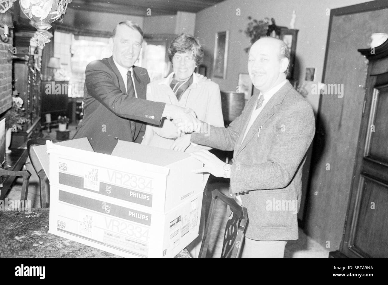 Présentation de la vidéo à la famille Engelkes gagnée avec un puzzle de Haarlems Dagblad Haarlems Dagblad etc. et IJmuider courant et cérémonie de remise des prix Koeri, Whizgle News, Dutch Desk, pays-Bas, 1950 - 2000 le 19-01-1984. Voici les rubriques de l'image. Dans un espace intérieur chaleureusement éclairé, trois individus se réunissent autour d’une table ornée de bois sombre riche, peut-être en acajou. L'ambiance semble amicale et festive, caractérisée par de larges sourires sur les visages des personnes impliquées. Sur la gauche, un homme en costume pointu serre la main à un autre homme qui porte une tenue plus décontractée mais bien taillée, Banque D'Images