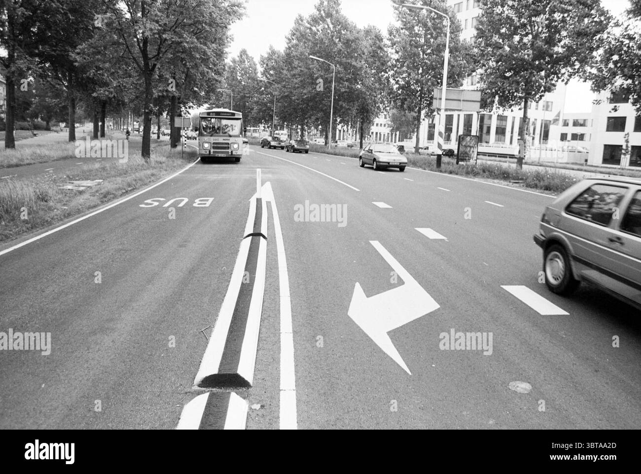 Rue avec voie de bus Haarlem Schalkwijk pays-Bas, Whizgle News, Dutch Desk, pays-Bas, 1950 - 2000 on 06-1992. L'image contient ces rubriques. La scène représente une rue de la ville située dans un environnement quelque peu urbain. La route est large, avec des voies divisées, avec des marquages distincts indiquant une voie de bus et des flèches directionnelles guidant la circulation. Sur le côté gauche du cadre, un bus approche, sa conception révélant un véhicule de transport public typique, tandis que plusieurs voitures sont vues plus près du premier plan, se déplaçant dans la direction opposée. Autour de la route, il y a des rangées de t Banque D'Images