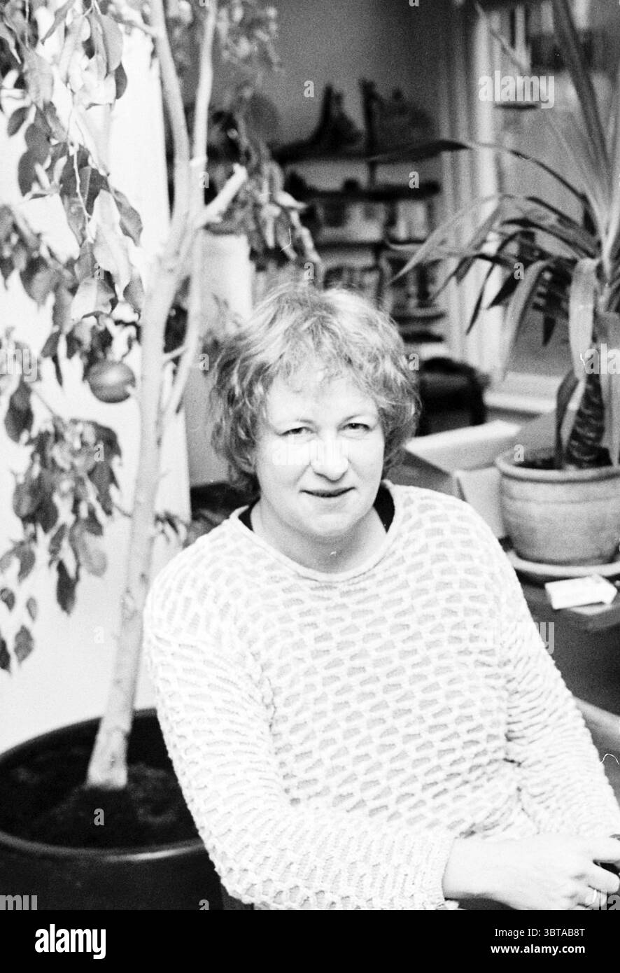 Janny Poelstra reçoit son doctorat Haarlem pays-Bas, Whizgle News, Dutch Desk, pays-Bas, 1950 - 2000 le 28-11-1996. L'image inclut ces rubriques. La scène met en scène une femme assise dans un espace intérieur confortable, encadré par la verdure. Elle a des cheveux bouclés, de couleur claire et porte un vêtement texturé, léger avec un motif subtil. L'expression sur son visage suggère la contemplation ou le calme. Autour d'elle sont des plantes en pot, y compris un petit arbre avec des feuilles vertes et peut-être quelques fruits, ajoutant une touche de vie au cadre. Les pots de plantes varient en taille et en couleur, certains présentant un ton terreux Banque D'Images