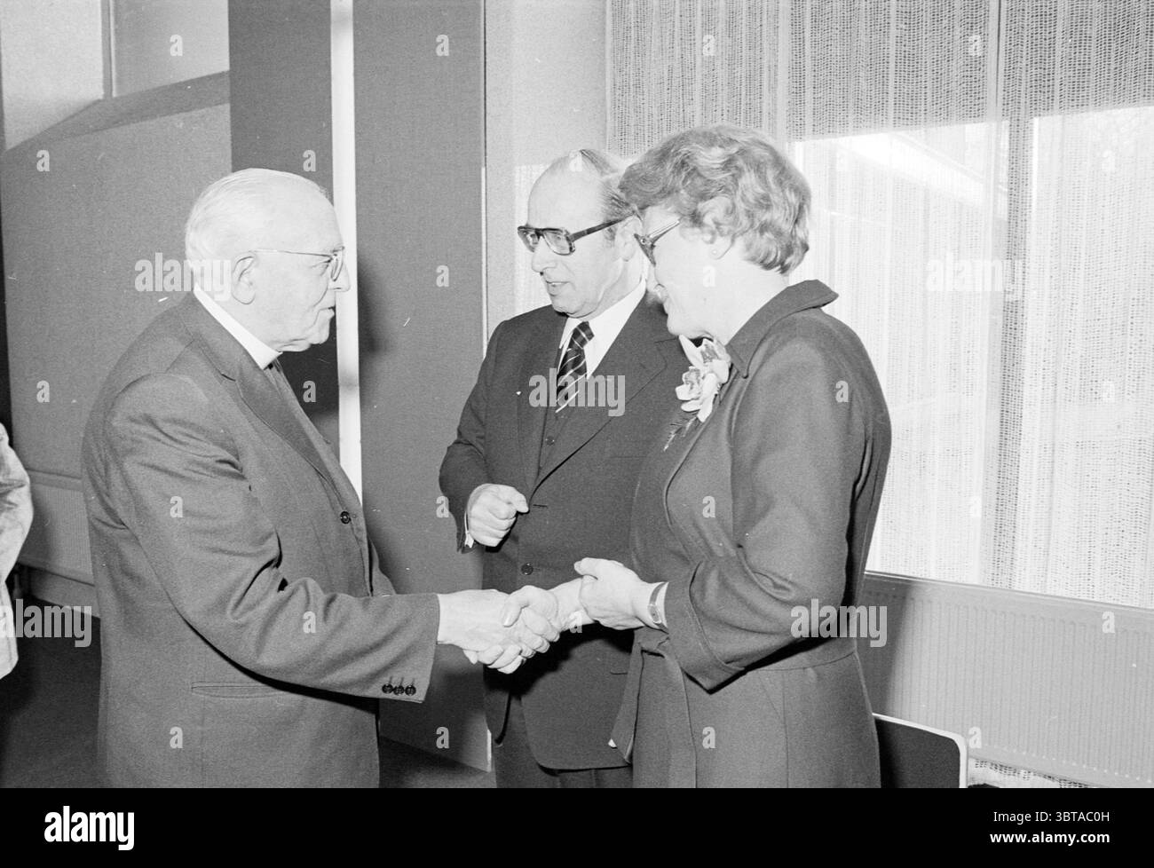 Réception d'adieu Dr van. Rhine Doctors Receptions, Whizgle News, Dutch Desk, pays-Bas, 1950 - 2000 on 10-12-1976. L'image montre ces rubriques. Dans un cadre formel, trois personnes sont engagées dans un moment d'interaction. La figure principale, un homme plus âgé avec des cheveux argentés et des lunettes, est positionnée sur la gauche. Il présente une expression digne et porte un costume sombre. Sa main est tendue dans une poignée de main, suggérant un geste de bienvenue ou d'accord. À sa droite se tient un autre homme, également vêtu d'un costume sombre et de lunettes, qui semble être en pleine conversation. Il reste légèrement tur Banque D'Images