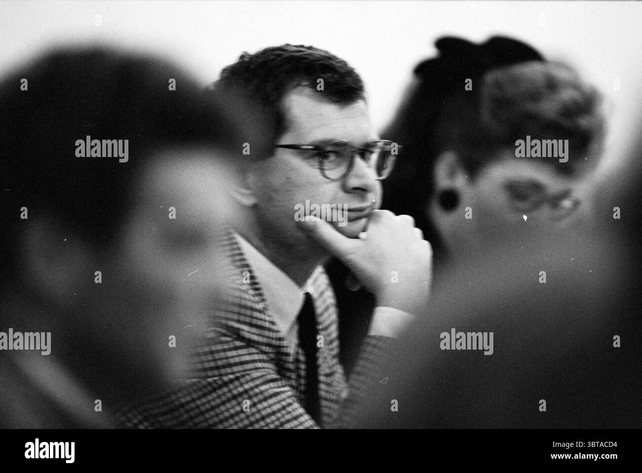 Budget Haarlem Haarlem pays-Bas, Whizgle News, Dutch Desk, pays-Bas, 1950 - 2000 le 15-11-1992. Ces rubriques sont illustrées dans l'image. La scène capture un rassemblement de personnes, probablement dans un cadre formel ou semi-formel. Au premier plan, un homme est assis avec son menton reposant réfléchi sur sa main, transmettant un sentiment de contemplation. Il porte des lunettes sombres à cadre métallique qui accentuent son expression pensive. Sa tenue est une veste à carreaux, qui ajoute une touche de style vintage. Derrière lui, les figures sont floues, créant un sentiment de profondeur et concentrant l'attention sur l'homme au premier plan. Banque D'Images