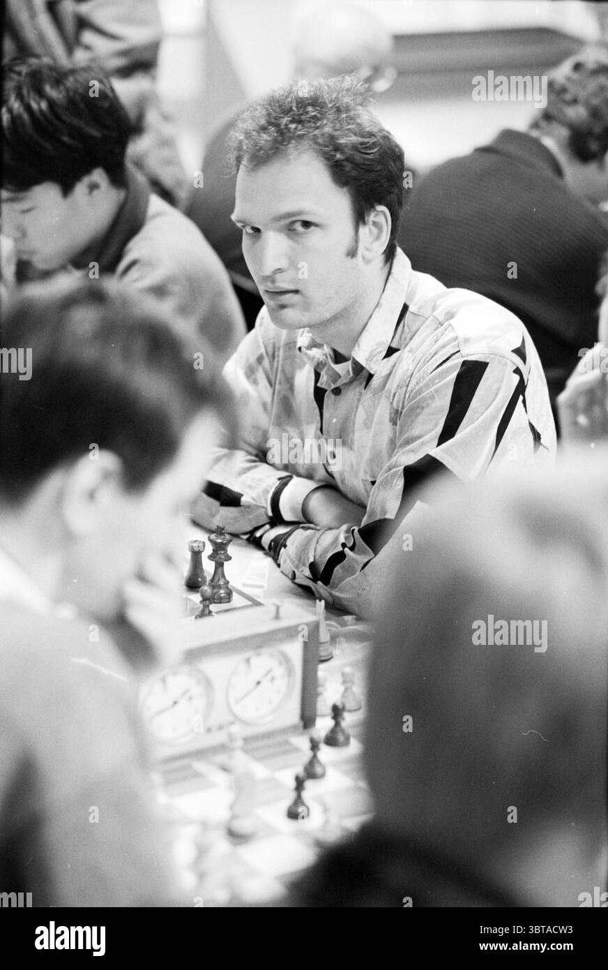 Échecs Heemstede Heemstede pays-Bas, Whizgle News, Dutch Desk, pays-Bas, 1950 - 2000 le 24-03-1995. L'image contient ces rubriques. Dans un cadre intérieur animé, un groupe d'individus est engagé dans une partie sérieuse d'échecs. L'accent est mis sur un homme avec une chemise rayée distinctive, avec des nuances de bleu clair et de noir. Son expression est intense et contemplative, suggérant une concentration profonde sur le jeu à portée de main. Autour de lui, d'autres joueurs se penchent sur leurs planches, leurs visages partiellement obscurcis. L'éclairage est neutre et légèrement sombre, créant une atmosphère sérieuse qui em Banque D'Images