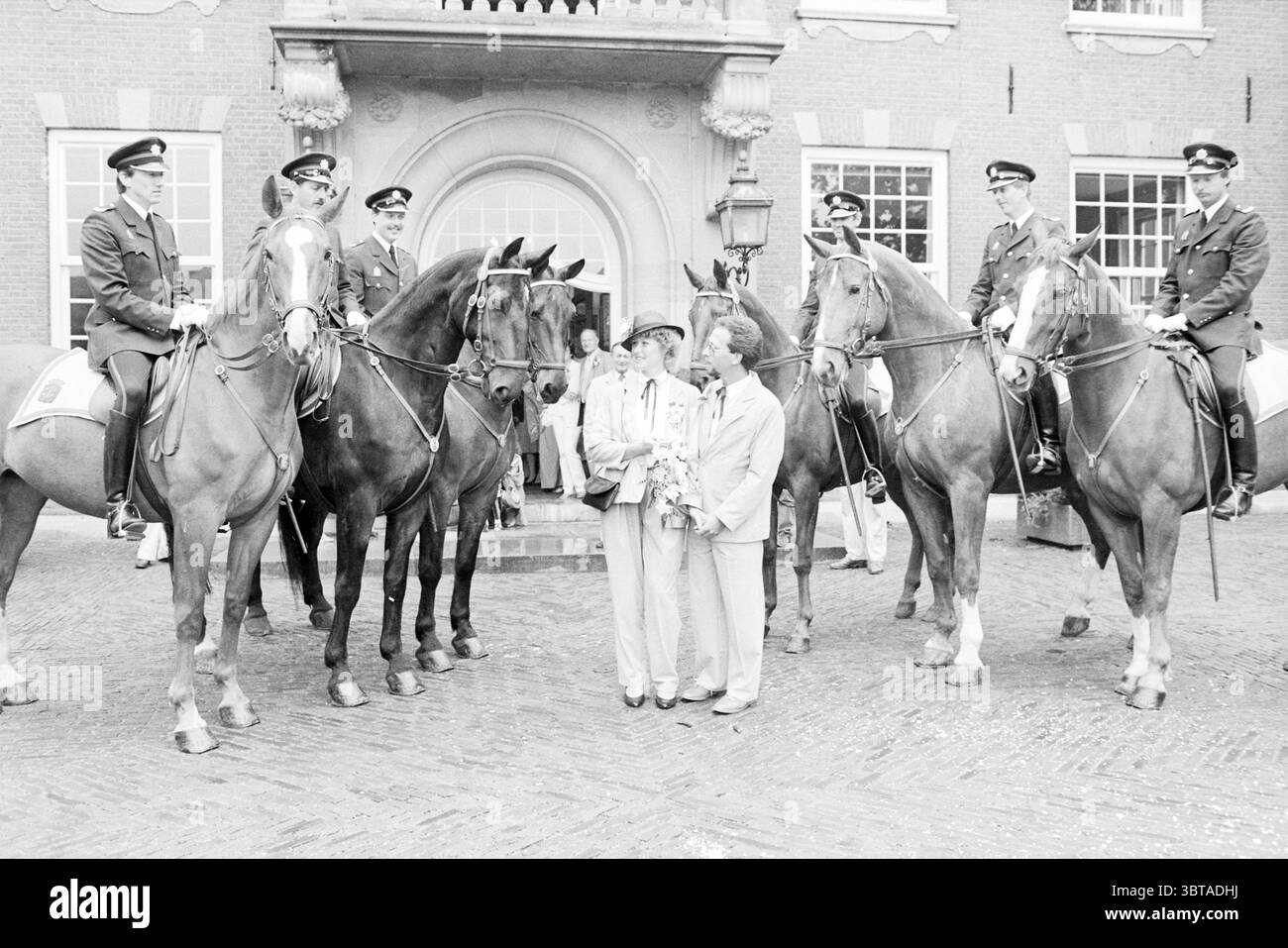 Officier de police monté de mariage avec garde d'honneur Heemstede police de mariage Heemstede pays-Bas, Whizgle News, Dutch Desk, pays-Bas, 1950 - 2000 le 29-06-1983. Ces rubriques sont illustrées dans l'image. Dans la scène, un groupe de six individus montés en uniforme se tient debout sur leurs chevaux, créant un ensemble visuel saisissant. Les chevaux sont robustes, avec des manteaux polis scintillant sous la douce lumière. Les cavaliers portent une tenue impeccable de style militaire, avec des casquettes qui correspondent au thème formel du décor. L'architecture environnante se vante d'un bâtiment majestueux avec des fenêtres symétriques Banque D'Images