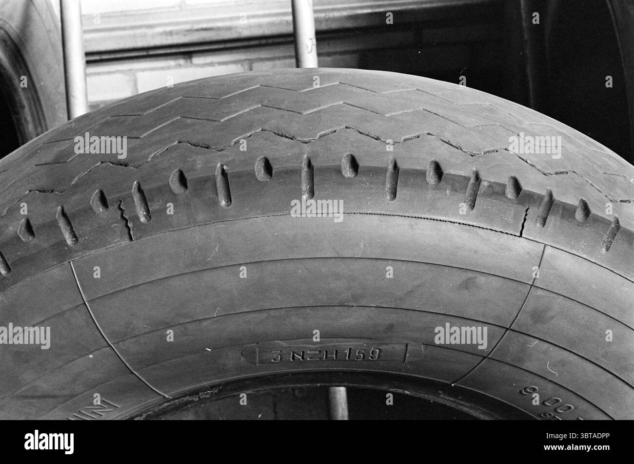 Pneus Noord Zuid Hollandse Vervoersmaatschappij N.V. NZ, Whizgle News, Dutch Desk, pays-Bas, 1950 - 2000 on 07-04-1964. Voici les rubriques de l'image. La scène est dominée par un grand pneu abîmé, sa surface texturée bien en vue. Le pneu présente une sculpture distincte avec des rainures profondes et une légère usure, ce qui indique qu'il a été utilisé de manière significative. Parmi les rainures, de petites fissures bordent la surface, suggérant l'âge et l'usure au fil du temps. Les couleurs sont atténuées, principalement des nuances de noir et de gris variables, avec des reflets qui captent la lumière, révélant les contours du pneu. Banque D'Images