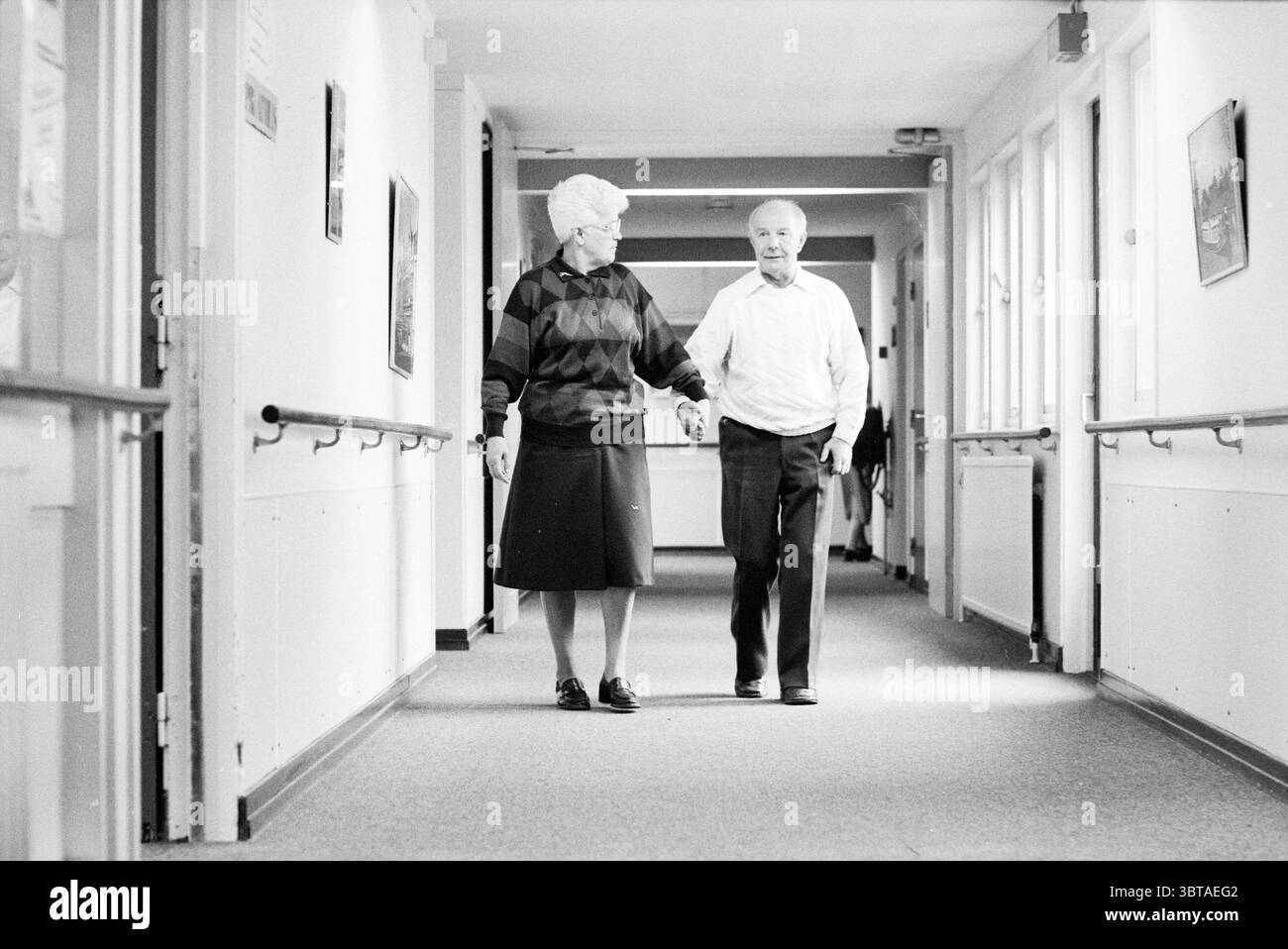 Rapport sur les maisons de soins Overspaarne maisons de soins Haarlem pays-Bas, Whizgle News, Dutch Desk, pays-Bas, 1950 - 2000 le 22-02-1988. Ce sont les éléments de l'image. Dans un couloir légèrement éclairé, deux personnes âgées marchent main dans la main, incarnant la chaleur et la compagnie. La femme, aux cheveux courts et blancs bien coiffés, porte un pull à motifs avec un mélange de couleurs vert foncé, bleu et rouille, jumelé avec une jupe noire qui tombe sous ses genoux. Ses chaussures sont sombres et pratiques, adaptées au cadre. À côté d'elle, l'homme a une tête défrisante gris clair et un sourire chaleureux qui ajoute Banque D'Images Rapport sur les maisons de soins Overspaarne maisons de soins Haarlem pays-Bas, Whizgle News, Dutch Desk, pays-Bas, 1950 - 2000 le 22-02-1988. Ce sont les éléments de l'image. Dans un couloir légèrement éclairé, deux personnes âgées marchent main dans la main, incarnant la chaleur et la compagnie. La femme, aux cheveux courts et blancs bien coiffés, porte un pull à motifs avec un mélange de couleurs vert foncé, bleu et rouille, jumelé avec une jupe noire qui tombe sous ses genoux. Ses chaussures sont sombres et pratiques, adaptées au cadre. À côté d'elle, l'homme a une tête défrisante gris clair et un sourire chaleureux qui ajoute Banque D'Images