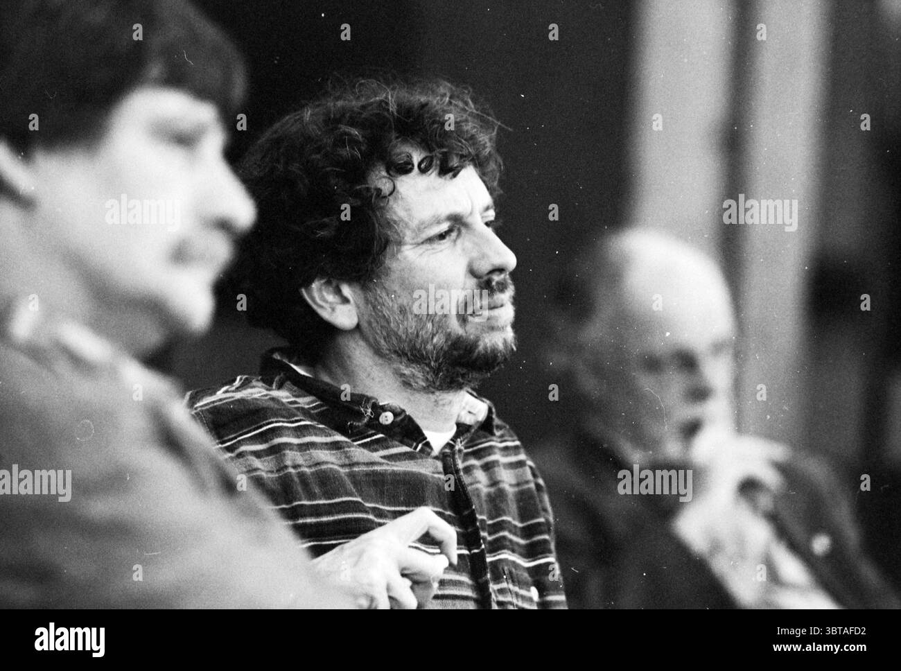 Budget H'Meer, Whizgle News, Dutch Desk, pays-Bas, 1950 - 2000 le 23-11-1994. L'image contient ces rubriques. Dans cette scène, trois individus sont assis en demi-cercle, créant une atmosphère dynamique et conversationnelle. La figure centrale a une expression réfléchie, avec des cheveux bouclés et une légère barbe, vêtue d'une chemise à carreaux qui présente un mélange de couleurs discrètes comme le vert, le brun et la crème. Sa posture est détendue mais engagée, ce qui suggère qu'il participe activement à la discussion en cours. La personne à sa droite a un comportement plus réservé, avec une moustache et portant un sol Banque D'Images