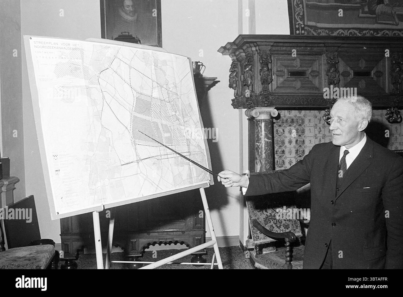 Conférence de presse Alderman appé Aldermen, Whizgle News, Dutch Desk, pays-Bas, 1950 - 2000 le 26-02-1968. Ces rubriques sont illustrées dans l'image. La scène représente un homme bien habillé faisant des gestes confiants vers une grande carte positionnée sur un chevalet. Il semble être dans un cadre formel, peut-être une salle de conférence ou un bureau riche en histoire. Les murs sont ornés de boiseries complexes, donnant un sens de la tradition et de l'importance au lieu. L'homme est habillé d'un costume sombre, qui contraste fortement avec son teint pâle. Ses cheveux sont soigneusement peignés, et il porte un ex sérieux mais animé Banque D'Images