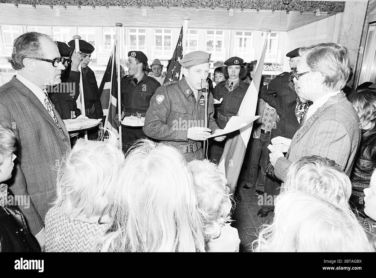 Célébration du 5 mai Velsen Torch run pseudo Canadian Liberation Day Liberation Fêtes de libération, Whizgle News, Dutch Desk, pays-Bas, 1950 - 2000 on 05-05-1975. L'image montre ces rubriques. Un groupe de personnes est réuni dans un cadre intérieur animé caractérisé par un design moderne avec de grandes fenêtres et une atmosphère lumineuse. Les hommes et les femmes vêtus d'une tenue habillée se tiennent étroitement ensemble, créant un sentiment de camaraderie et de but. Au premier plan, une personne en uniforme, probablement un leader ou un orateur, tient un document et s'adresse à l'Assemblée. Son comportement est sérieux mais valide Banque D'Images
