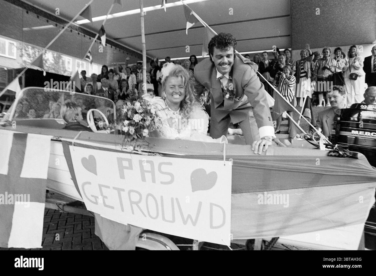 Se marier à 't Bootje Velsen Town Hall Velsen, Whizgle News, Dutch Desk, pays-Bas, 1950 - 2000 le 27-08-1992. L'image montre ces rubriques. Dans la scène, un couple jubilant est positionné à l'avant-garde, exsudant le bonheur alors qu'ils célèbrent leur union. Le marié, vêtu d'un costume gris clair, se penche légèrement hors d'un bateau décoré, un large sourire qui s'étend sur son visage. Ses cheveux sont coiffés d'une manière volumineuse, ajoutant à son comportement expressif. À côté de lui, la mariée captive avec son élégante robe blanche, qui présente des détails délicats en tissu. Ses cheveux sont elegantl Banque D'Images