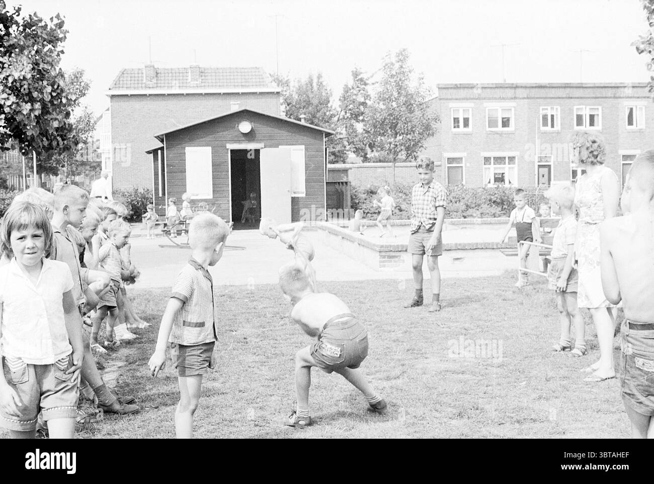 Jeux et compétitions en terrain de jeux de vacances Elba jours de vacances camp de vacances, Whizgle News, Dutch Desk, pays-Bas, 1950 - 2000 le 22-07-1963. Ce sont les éléments de l'image. Dans un cadre extérieur ensoleillé, un groupe d’enfants joue énergiquement sur une étendue herbeuse, leur enthousiasme palpable dans les airs. La scène est vivante de rire et de mouvement. Sur le côté gauche, un groupe d'enfants, certains avec les cheveux coupés étroitement, observent attentivement tandis que d'autres s'engagent dans des cabrioles ludiques. Leurs vêtements sont légers et estivaux, avec des manches courtes et des shorts, faisant allusion à une journée chaude. Les couleurs de t Banque D'Images