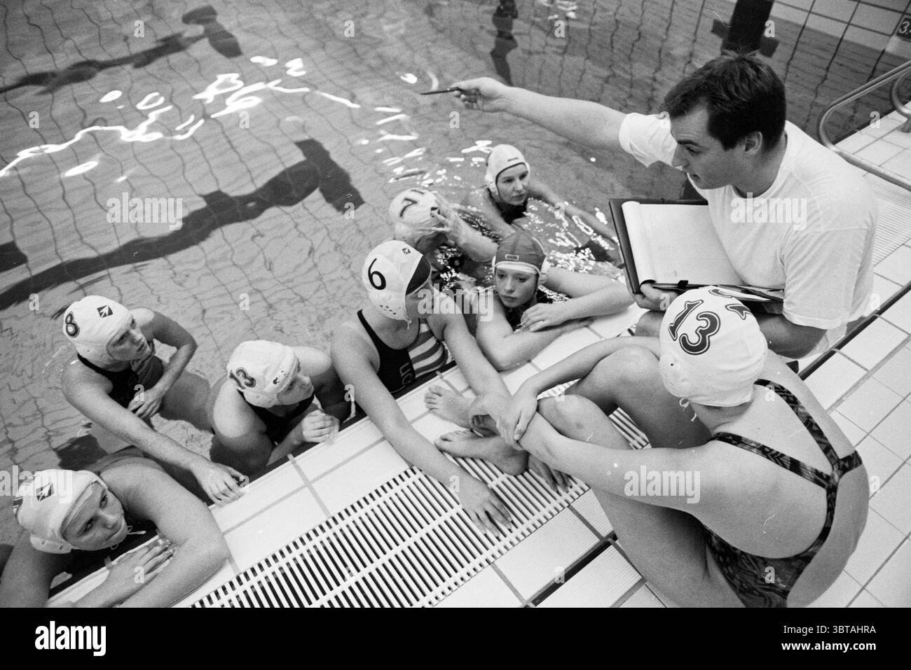 Entraîneur féminin VVA Marcel, Whizgle News, Dutch Desk, pays-Bas, 1950 - 2000 le 06-10-1992. Ce sont les éléments de l'image. Dans un cadre aquatique très éclairé, un groupe d’individus est rassemblé au bord d’une piscine. La scène capture un moment de discussion, probablement une séance de coaching pour une équipe de water-polo. L'eau est d'un bleu éclatant, créant un contraste frappant avec les couleurs tamisées de la terrasse de la piscine carrelée, qui est principalement blanche avec des notes de gris. Le groupe se compose de plusieurs femmes, chacune portant des bonnets de bain assortis - certains de couleurs Unies et d'autres avec des chiffres, indiquant Banque D'Images
