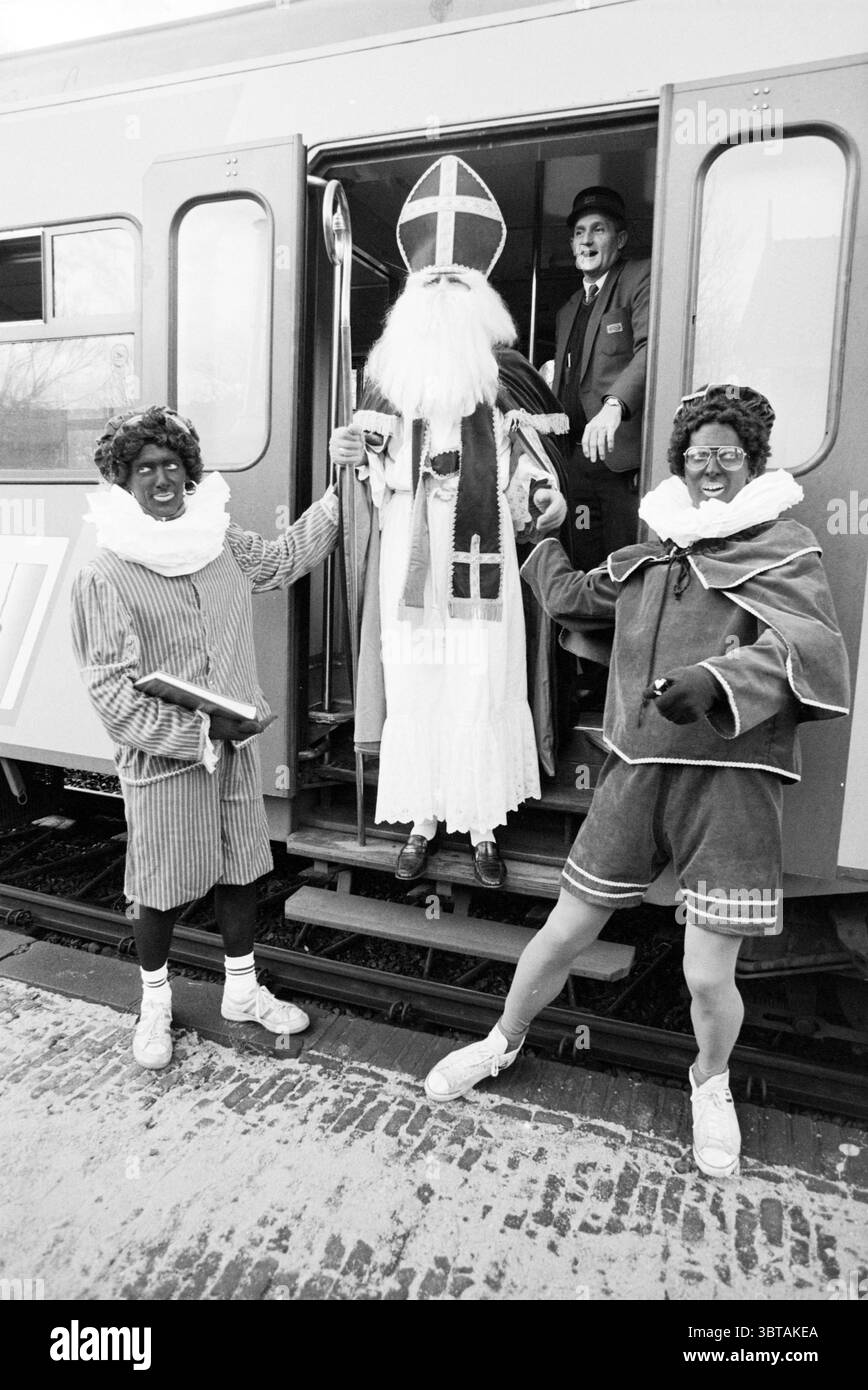 Arrivée de Saint Nicholas à Vogelenzang : Nicholas Sinterklaas Vogelenzang, Whizgle News, Dutch Desk, pays-Bas, 1950 - 2000 on 19-11-1988. L'image contient ces rubriques. La scène présente un moment rempli d'énergie festive et de personnages ludiques. Au premier plan, trois individus sont bien en évidence, vêtus de costumes colorés. La figure centrale, incarnant un personnage de vacances traditionnel, porte une longue robe fluide en blanc, ornée d'embellissements rouges et dorés. Un grand onglet pointu couronne leur tête, tandis qu'une longue barbe blanche obscurcit une grande partie de leur visage. Ils gra Banque D'Images