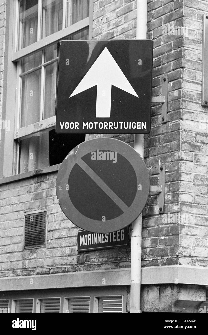 Panneaux de signalisation pour la circulation à sens unique et le stationnement interdit Morinnesteeg corner Smedestraat Haarlem Morinnesteeg pays-Bas., Whizgle News, Dutch Desk, pays-Bas, 1950 - 2000. Ces rubriques apparaissent dans l'image. Dans la scène, il y a plusieurs signes affichés en évidence, qui se détachent contre un mur de briques texturé. Le panneau principal, situé en haut, comporte une flèche audacieuse pointant vers le haut, suggérant la direction. Il est placé sur un fond noir dur, améliorant sa visibilité. En dessous de cette flèche, un panneau circulaire avec une bordure rouge indique une interdiction, signalant probablement ce stationnement Banque D'Images