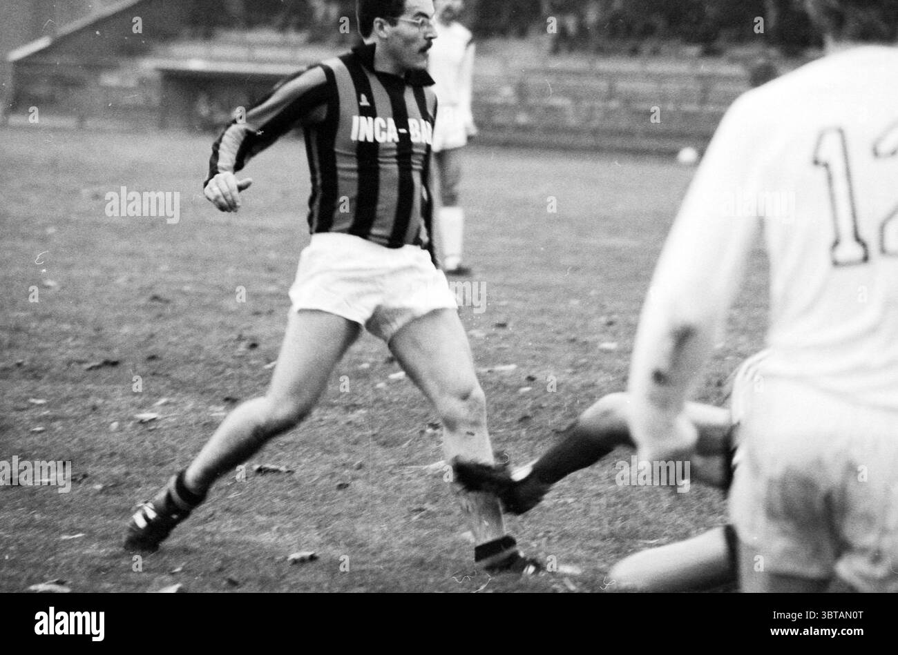 RCH - KIC Football R.C.H., Whizgle News, Dutch Desk, pays-Bas, 1950 - 2000 le 22-10-1982. L'image contient ces rubriques. Dans une scène sportive dynamique, deux joueurs s’engagent dans un moment intense d’un match de football. Un joueur, vêtu d'un maillot rayé noir et rouge saisissant, est dans une pose dynamique, réagissant apparemment au jeu qui se déroule autour de lui. Son expression transmet la détermination, avec des sourcils sillonnés et une bouche ouverte qui suggère qu'il crie peut-être ou élabore une stratégie. Le cadre présente un champ herbeux, avec des taches de vert clair et plus foncé visibles, indiquant l'usure de la précédente gammie Banque D'Images RCH - KIC Football R.C.H., Whizgle News, Dutch Desk, pays-Bas, 1950 - 2000 le 22-10-1982. L'image contient ces rubriques. Dans une scène sportive dynamique, deux joueurs s’engagent dans un moment intense d’un match de football. Un joueur, vêtu d'un maillot rayé noir et rouge saisissant, est dans une pose dynamique, réagissant apparemment au jeu qui se déroule autour de lui. Son expression transmet la détermination, avec des sourcils sillonnés et une bouche ouverte qui suggère qu'il crie peut-être ou élabore une stratégie. Le cadre présente un champ herbeux, avec des taches de vert clair et plus foncé visibles, indiquant l'usure de la précédente gammie Banque D'Images