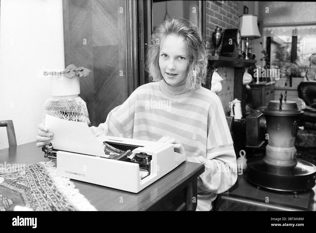 Examen ester Lammers candidat examen, Whizgle News, Dutch Desk, pays-Bas, 1950 - 2000 le 22-07-1988. Ce sont les éléments de l'image. La scène montre une jeune femme assise à une table en bois, engagée dans la dactylographie sur une machine à écrire. Elle a les cheveux légèrement touffus et porte un pull rayé qui crée un contraste doux sur le fond. Les rayures alternent entre les nuances claires et sombres, apportant une touche décontractée mais élégante à son apparence. La machine à écrire, modèle classique, se tient bien en vue sur la table, son corps blanc élégant contrastant avec la richesse du bois. Dispersé a Banque D'Images Examen ester Lammers candidat examen, Whizgle News, Dutch Desk, pays-Bas, 1950 - 2000 le 22-07-1988. Ce sont les éléments de l'image. La scène montre une jeune femme assise à une table en bois, engagée dans la dactylographie sur une machine à écrire. Elle a les cheveux légèrement touffus et porte un pull rayé qui crée un contraste doux sur le fond. Les rayures alternent entre les nuances claires et sombres, apportant une touche décontractée mais élégante à son apparence. La machine à écrire, modèle classique, se tient bien en vue sur la table, son corps blanc élégant contrastant avec la richesse du bois. Dispersé a Banque D'Images