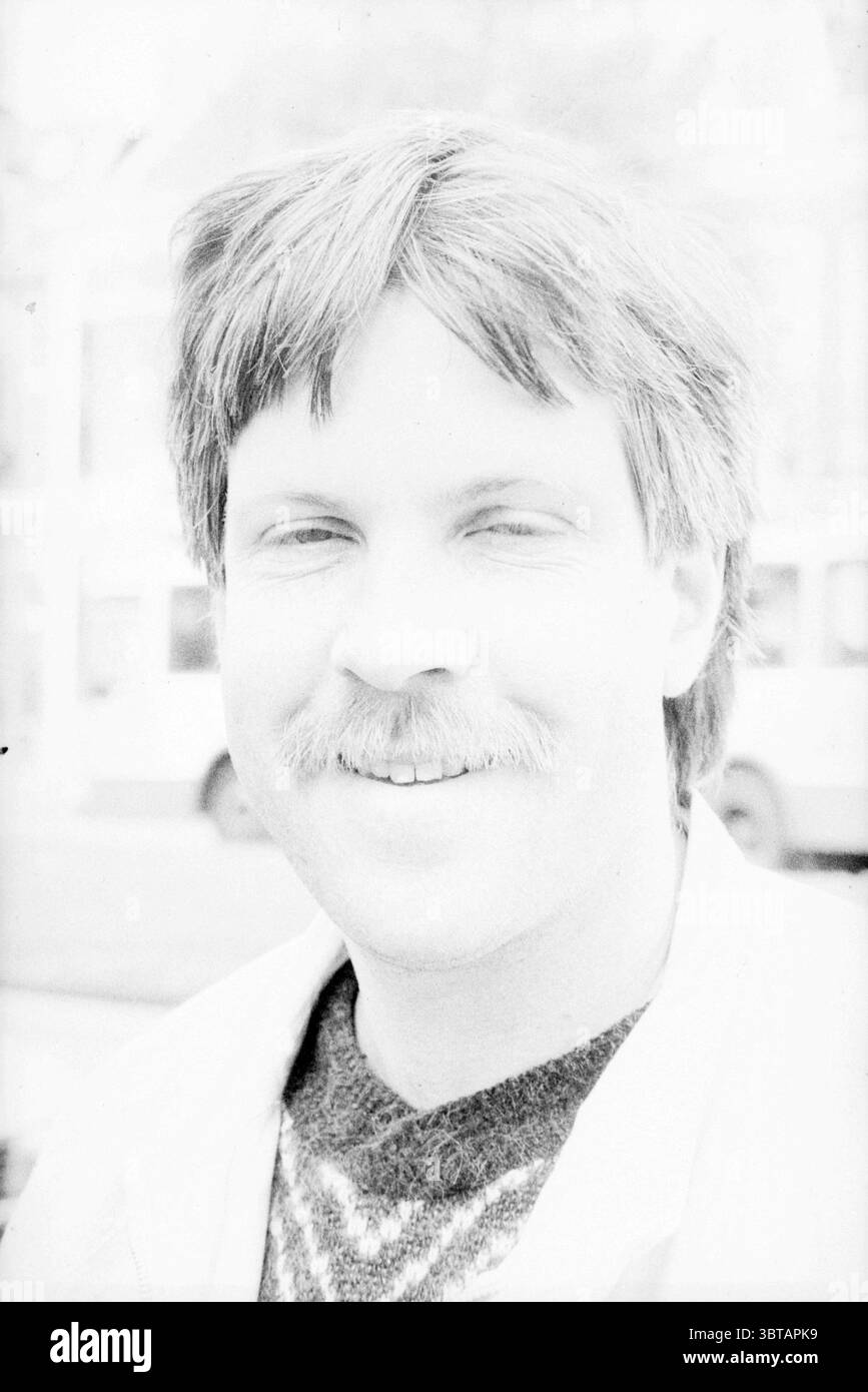 Portraits Portraits Talk of the day, Whizgle News, Dutch Desk, pays-Bas, 1950 - 2000 sur 05-05-1988. Voici les rubriques de l'image. Dans la scène, un homme au teint clair est en évidence. Il a des cheveux légèrement touffus à la longueur des épaules, avec une teinte plus foncée aux racines qui passe à une teinte plus claire. Son expression faciale transmet chaleur et convivialité, soulignée par un sourire léger et content. Une moustache ajoute à son comportement accessible. Il porte une veste de couleur claire sur un pull à motifs, suggérant un style décontracté mais assemblé. Le motif sur le pull Banque D'Images