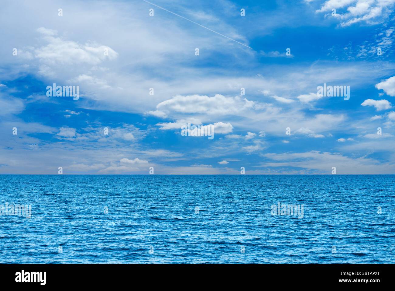 Vaste vue sur l'océan sous un ciel bleu lumineux avec des nuages blancs moelleux, paysage marin serein Banque D'Images