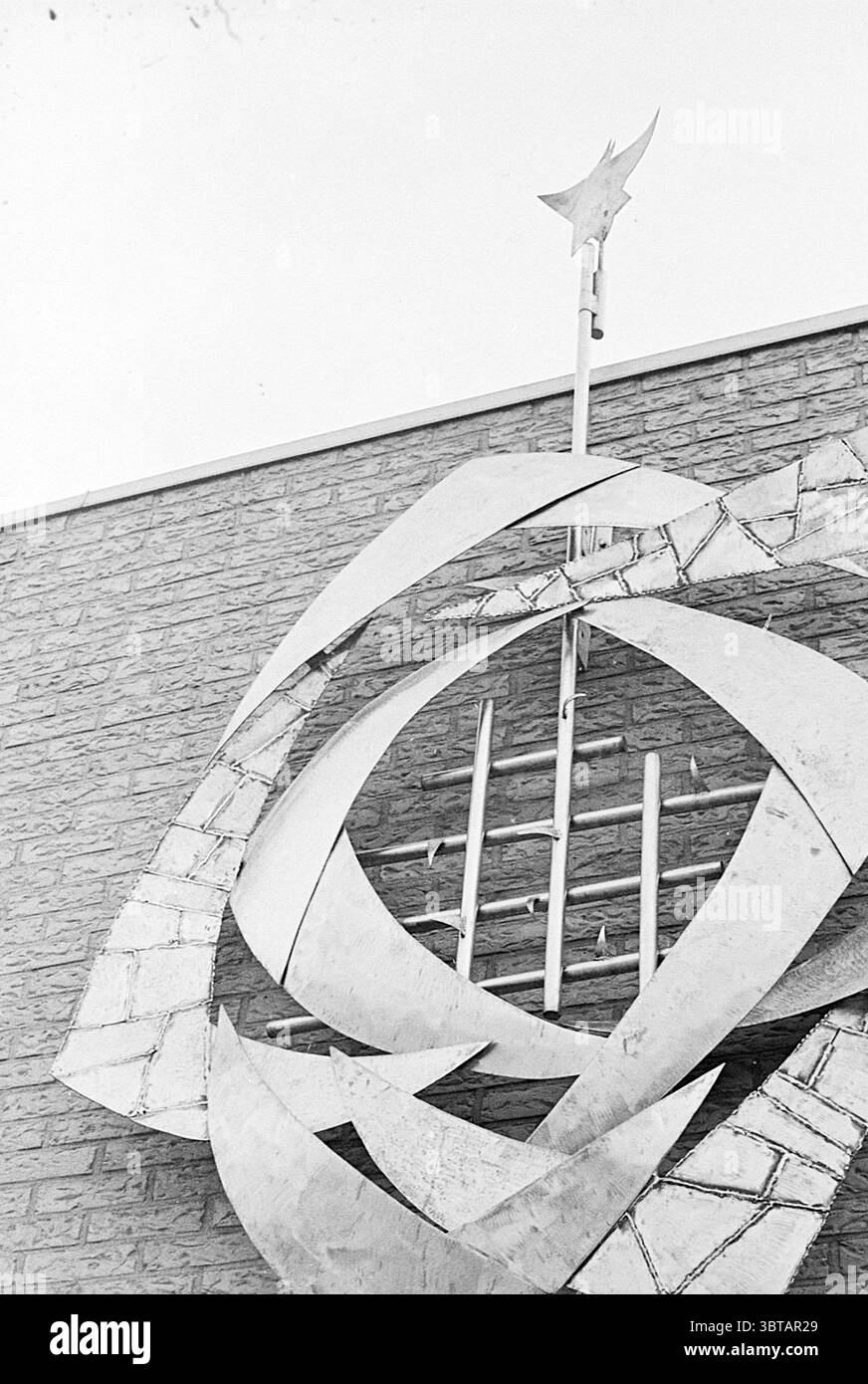 Façade Anne Frank School Heemskerk Jan van Kuikweg., Whizgle News, Dutch Desk, pays-Bas, 1950 - 2000. Ces rubriques apparaissent dans l'image. La scène présente une grande sculpture abstraite en métal montée sur un mur de pierre texturé. La sculpture présente des formes sinueuses et larges qui se tordent et se croisent, créant une sensation de mouvement et de dynamisme. La surface métallique réfléchit la lumière, présentant un mélange de finitions polies et mates qui améliorent sa qualité tridimensionnelle. Au sommet de la sculpture, une forme allongée, en forme d'étoile, fait saillie vers le haut, attirant le regard. Ci-dessous, une série de courbes et d'angul Banque D'Images Façade Anne Frank School Heemskerk Jan van Kuikweg., Whizgle News, Dutch Desk, pays-Bas, 1950 - 2000. Ces rubriques apparaissent dans l'image. La scène présente une grande sculpture abstraite en métal montée sur un mur de pierre texturé. La sculpture présente des formes sinueuses et larges qui se tordent et se croisent, créant une sensation de mouvement et de dynamisme. La surface métallique réfléchit la lumière, présentant un mélange de finitions polies et mates qui améliorent sa qualité tridimensionnelle. Au sommet de la sculpture, une forme allongée, en forme d'étoile, fait saillie vers le haut, attirant le regard. Ci-dessous, une série de courbes et d'angul Banque D'Images