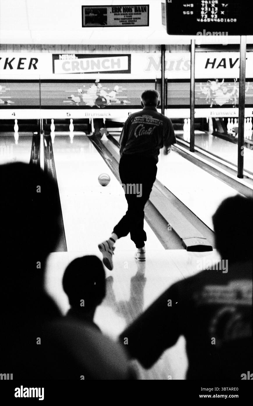 Bowling Claus Party House, Whizgle News, Dutch Desk, pays-Bas, 1950 - 2000 sur 14-01-1995. L'image contient ces rubriques. La scène se déroule dans une piste de bowling animée, caractérisée par une atmosphère animée. Le point focal est un bowler dans une chemise bleue, capturé à mi-action alors qu'ils relâchent une boule de bowling vers les quilles devant. Leur position est confiante, avec un pied légèrement en avant et la jambe arrière bien fixée, indiquant la force du lancer. En arrière-plan, des néons lumineux ajoutent une lueur colorée à la scène, reflétant les ruelles en bois poli. Les quilles de bowling se tiennent avec défiance à la Banque D'Images