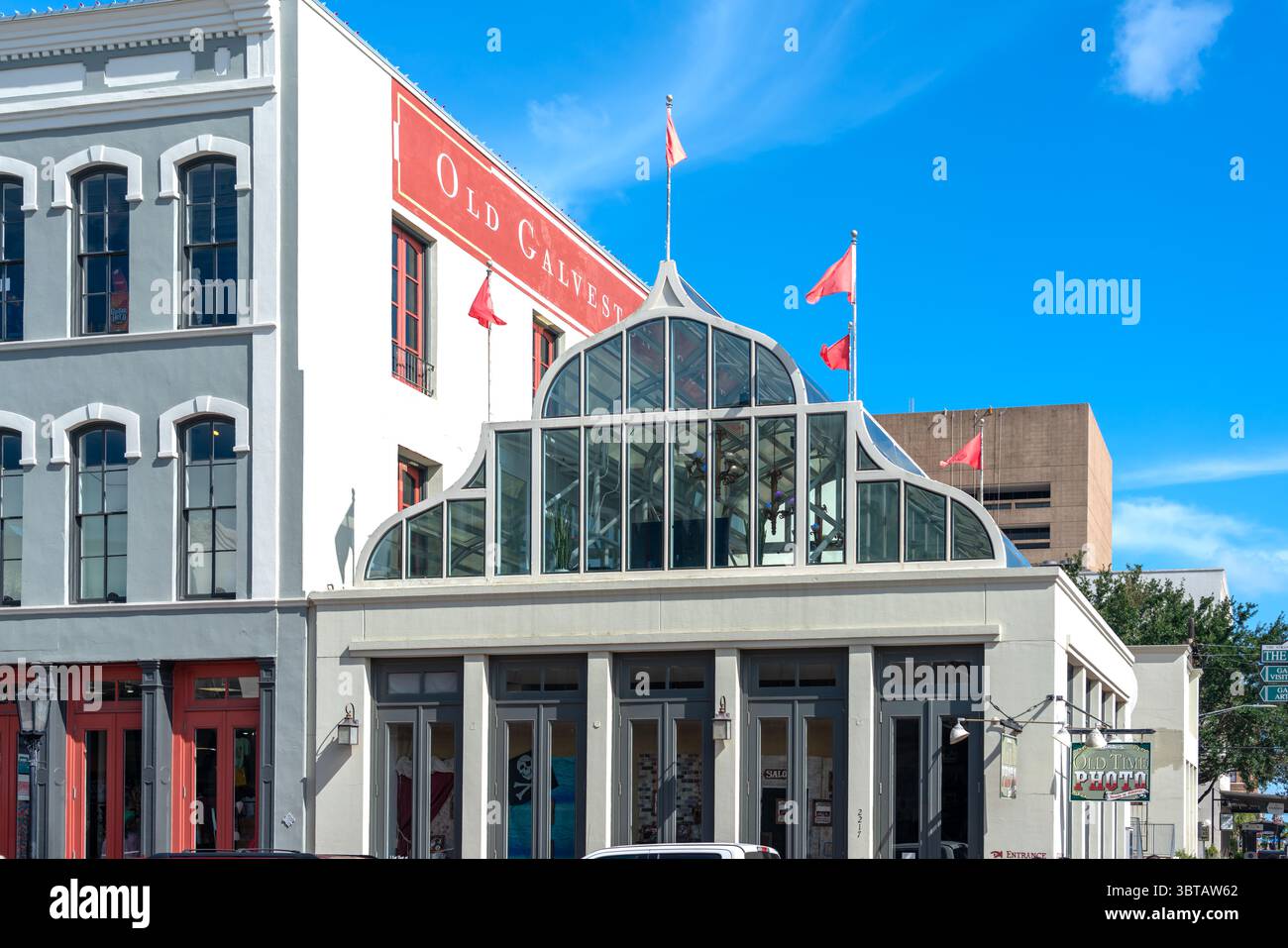 Galveston, États-Unis - 11 juillet 2025 : ancien bâtiment de Galveston Square avec entrée pavillon en verre et drapeaux rouges Banque D'Images