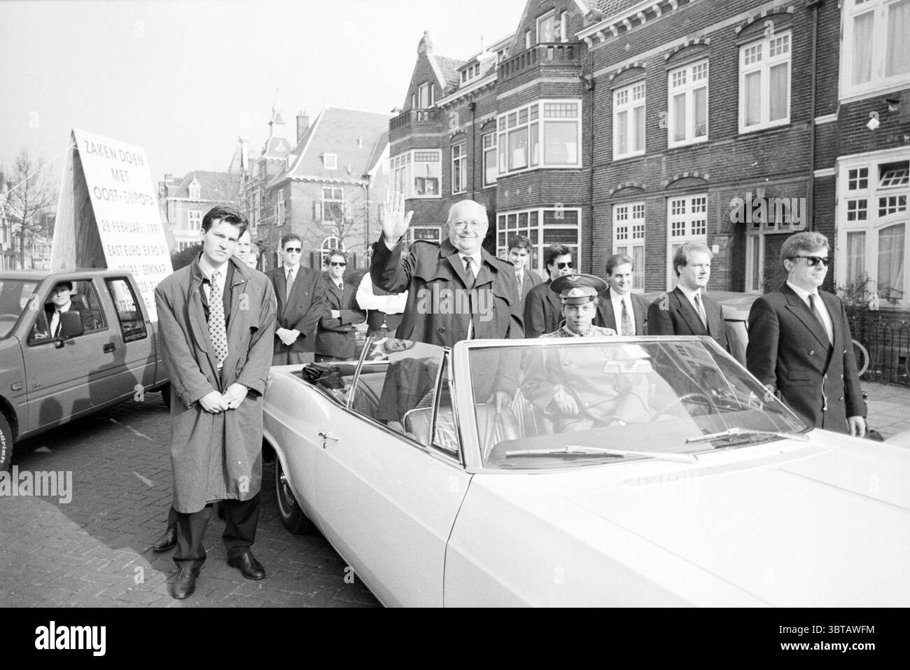 Publicité pour 'East Euro Expo 1991' défilé de voitures avec le look-like Gorbatchev Haarlem pays-Bas, Whizgle News, Dutch Desk, pays-Bas, 1950 - 2000 sur 25-02-1991. Ce sont les éléments de l'image. Dans un cadre urbain animé, un cabriolet classique est garé en évidence, sa capote vers le bas, révélant l'intérieur et un groupe de personnages. Le véhicule est d'une couleur claire, contrastant avec les tons foncés des bâtiments en briques à l'arrière-plan, qui présentent de grandes fenêtres et des éléments décoratifs typiques de l'architecture traditionnelle. Un homme plus âgé distingué, portant un costume sombre, fait des vagues Banque D'Images