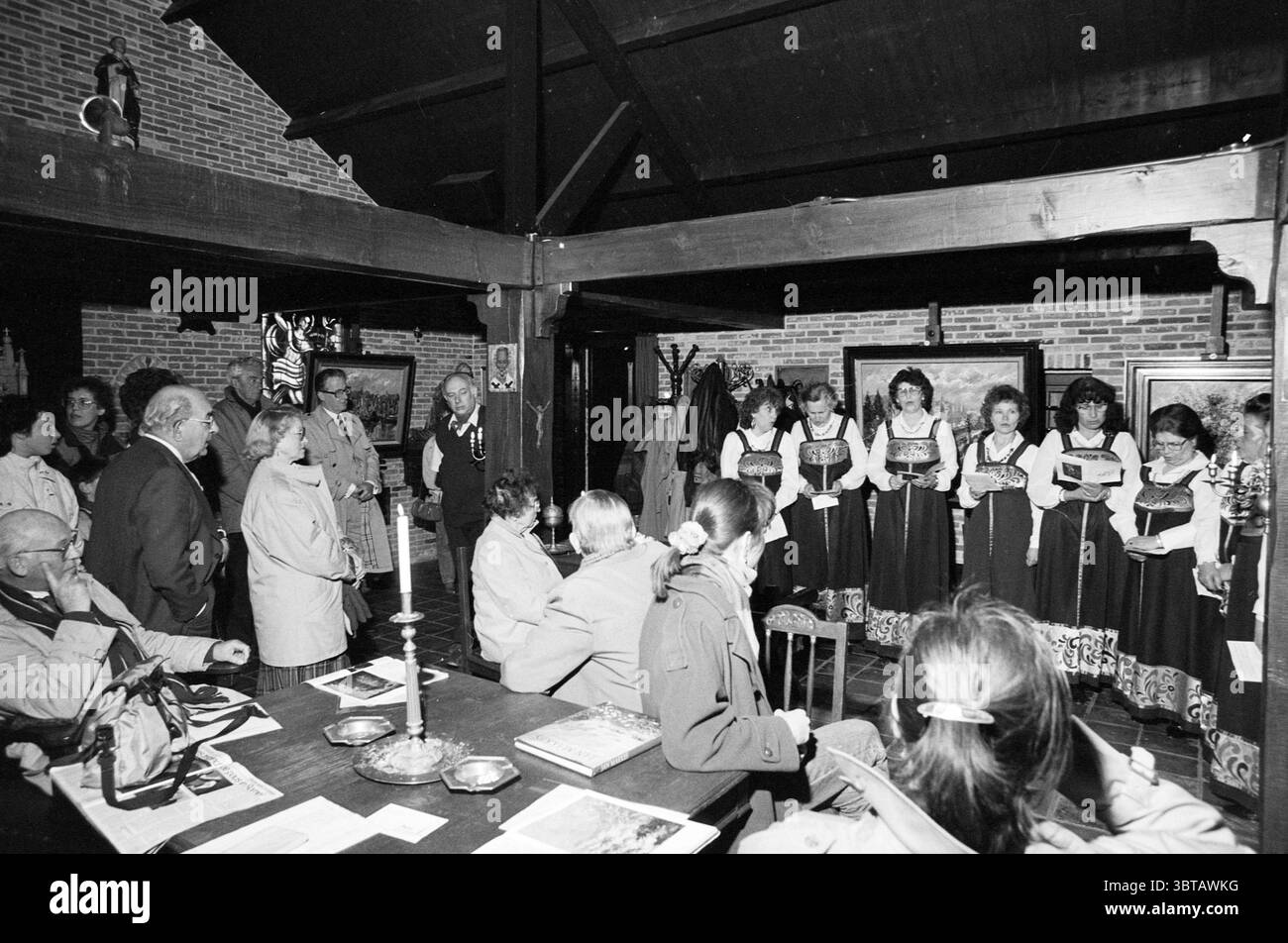 Chorale russe avec Jan Makkes Koren, Whizgle News, Dutch Desk, pays-Bas, 1950 - 2000 le 02-04-1989. L'image contient ces rubriques. La scène se déroule dans un cadre intérieur rustique caractérisé par des poutres apparentes et des murs de briques, véhiculant une atmosphère chaleureuse et accueillante. L'éclairage tamisé crée une ambiance chaleureuse, contrastant doucement avec la luminosité de la tenue des participants. Un groupe de femmes se tient bien en vue au premier plan, vêtues de robes traditionnelles qui présentent des motifs complexes et des couleurs vibrantes, principalement des nuances de noir et blanc, accentuées de riches teintes. Leurs expres Banque D'Images