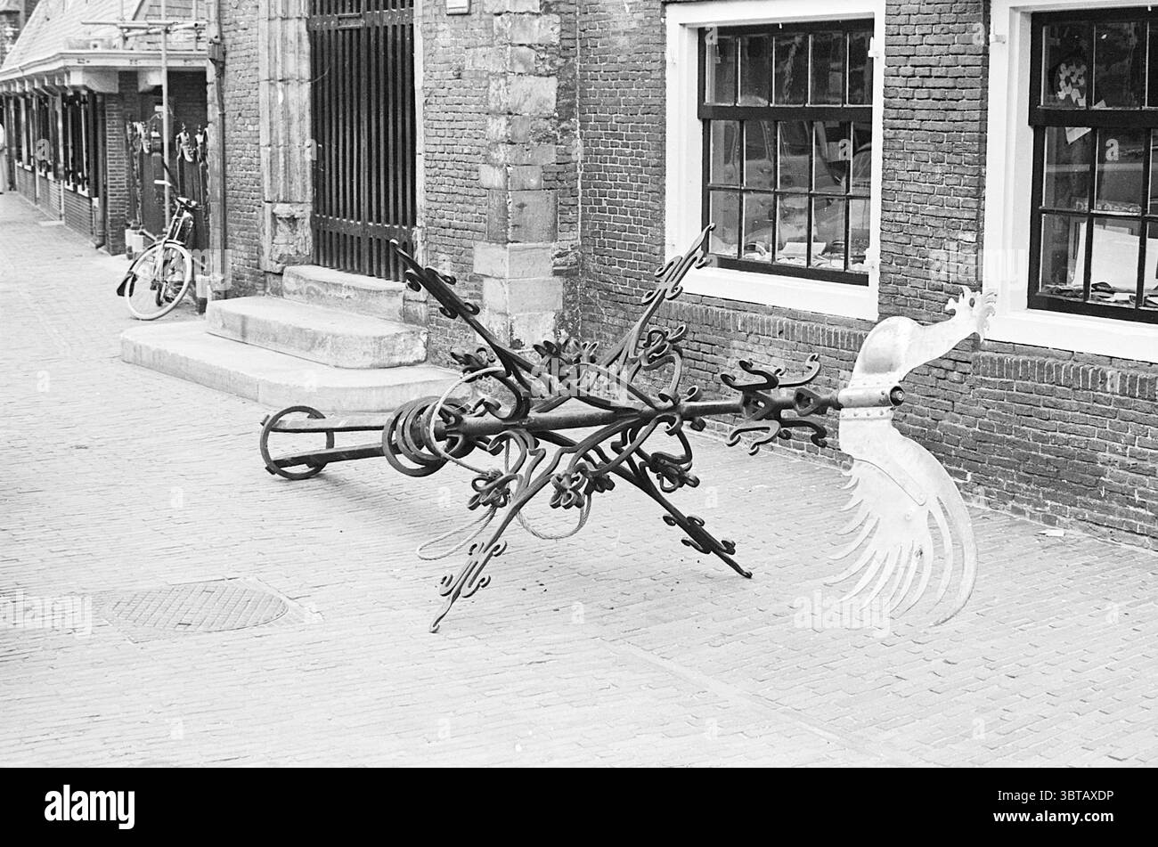 Collecte de la croix et du coq Grote ou Sint-Bavokerk Grote Kerk Haarlem églises Bavokerk Haarlem Grote Markt pays-Bas, Whizgle News, Dutch Desk, pays-Bas, 1950 - 2000 on 30-06-1964. Ce sont les éléments de l'image. La scène capture une rue étroite et pavée bordée de bâtiments traditionnels en briques, présentant des caractéristiques architecturales d'une époque révolue. Les bâtiments ont de grandes fenêtres à plusieurs vitres qui reflètent la lumière ambiante, ajoutant de la profondeur à la scène. Au premier plan, une sculpture métallique complexe semble être un mélange d'éléments décoratifs et fonctionnels. Il h Banque D'Images Collecte de la croix et du coq Grote ou Sint-Bavokerk Grote Kerk Haarlem églises Bavokerk Haarlem Grote Markt pays-Bas, Whizgle News, Dutch Desk, pays-Bas, 1950 - 2000 on 30-06-1964. Ce sont les éléments de l'image. La scène capture une rue étroite et pavée bordée de bâtiments traditionnels en briques, présentant des caractéristiques architecturales d'une époque révolue. Les bâtiments ont de grandes fenêtres à plusieurs vitres qui reflètent la lumière ambiante, ajoutant de la profondeur à la scène. Au premier plan, une sculpture métallique complexe semble être un mélange d'éléments décoratifs et fonctionnels. Il h Banque D'Images