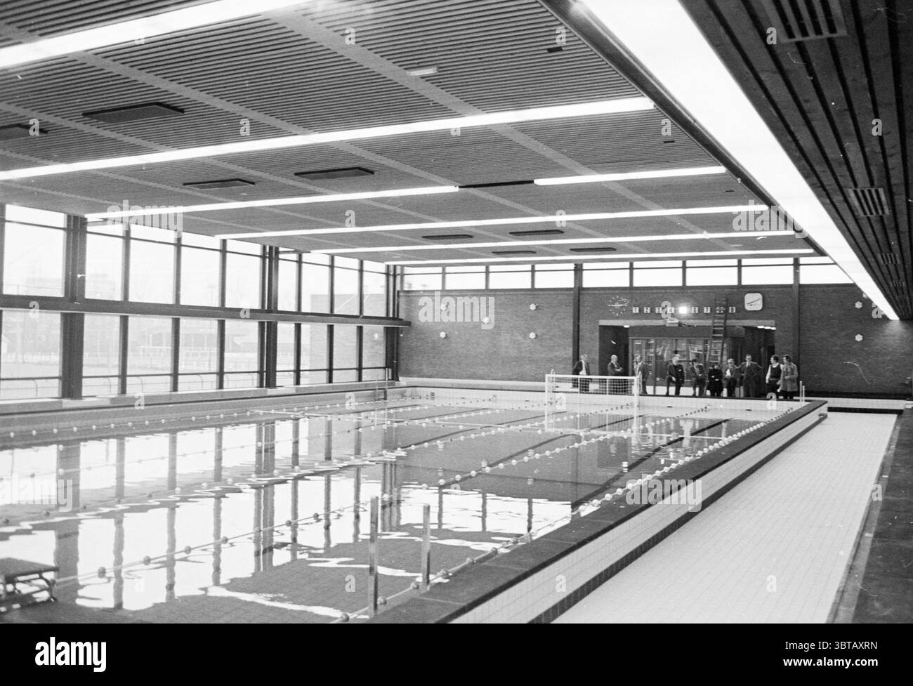 Piscine intérieure 'de Planet' Haarlem Planetenlaan pays-Bas, Whizgle News, Dutch Desk, pays-Bas, 1950 - 2000 on 12-1971. Ce sont les éléments de l'image. La scène représente une piscine intérieure, caractérisée par son architecture spacieuse et moderne. De grandes fenêtres s'étendent sur un côté, permettant à une grande lumière naturelle d'inonder la zone, créant une atmosphère lumineuse et aérée. La piscine elle-même est remplie d'eau chatoyante, reflétant l'éclairage aérien et l'environnement environnant. Les murs sont construits à partir de briques lisses brunes, offrant un contraste chaleureux avec le Banque D'Images