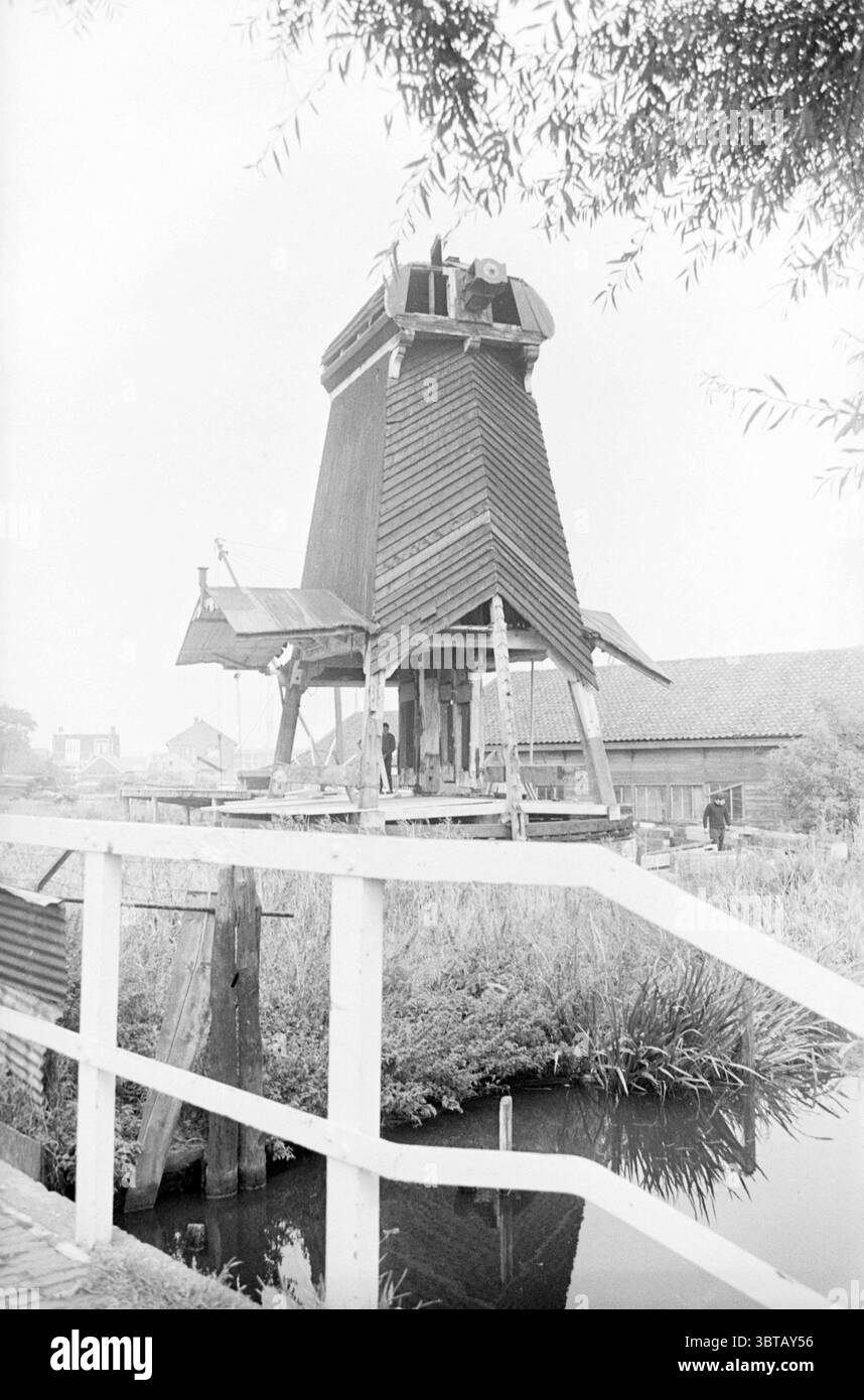 Restauration du moulin 'de Eenhoorn'. Haarlem Zuid Schalkwijkerweg 6F pays-Bas, Whizgle News, Dutch Desk, pays-Bas, 1950 - 2000 en 1967. L'image montre ces rubriques. La scène représente un moulin à vent rustique, caractérisé par sa structure traditionnelle en bois et un toit triangulaire distinct. Le moulin à vent se trouve sur une légère élévation, entouré d'un paysage vibrant rempli de hautes herbes et de feuillage sauvage. Un plan d'eau serein reflète doucement le moulin à vent, améliorant l'ambiance tranquille du cadre. Le moulin à vent lui-même a un aspect altéré, montrant des signes d'âge avec son Banque D'Images