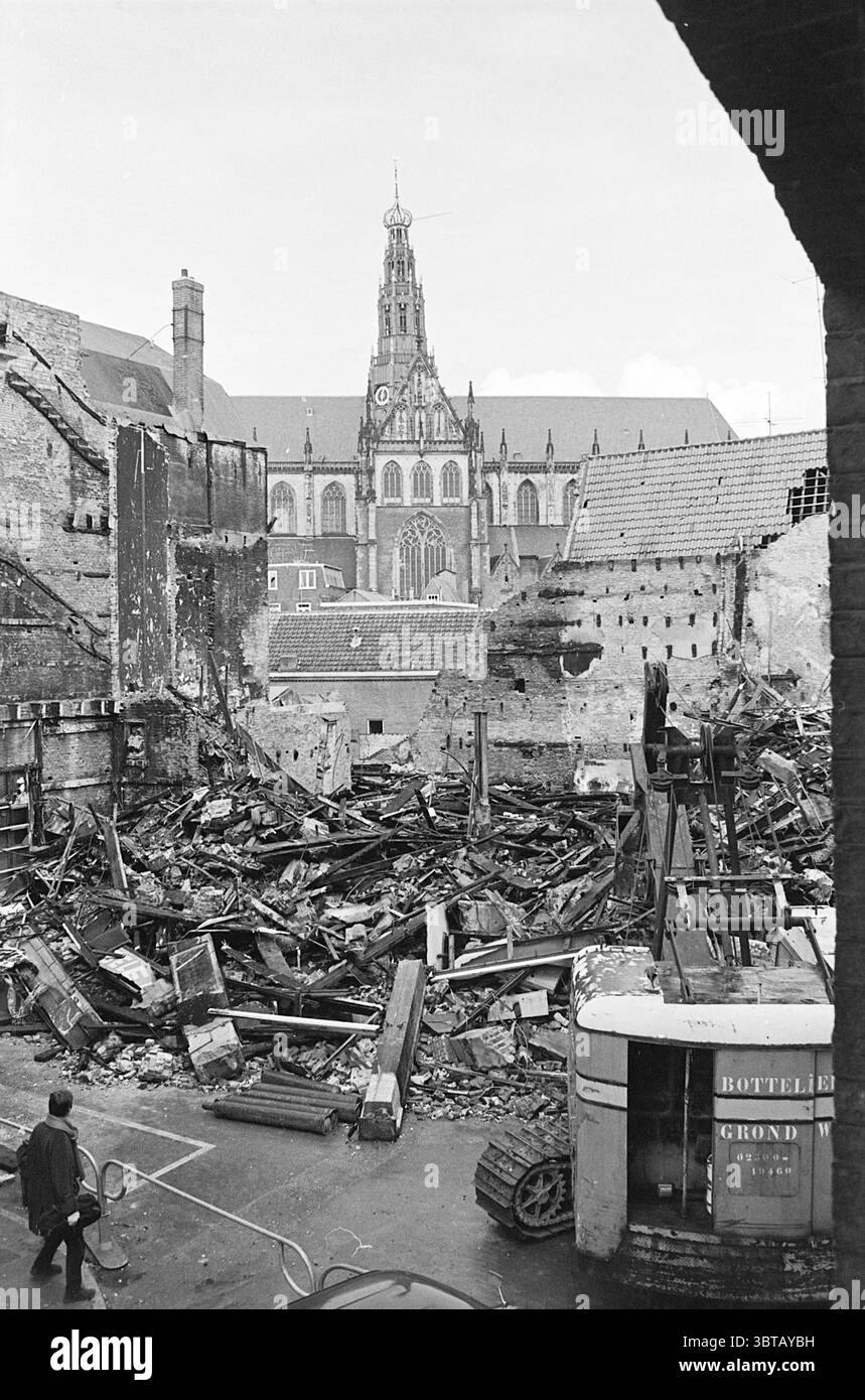 Démolition après incendie Schagchelstraat Haarlem pays-Bas, Whizgle News, Dutch Desk, pays-Bas, 1950 - 2000 on 07-04-1970. L'image contient ces rubriques. La scène capture un décor sombre et sombre, caractérisé par la dévastation et les vestiges de ce qui était autrefois un espace vibrant. Au premier plan, des tas de bois carbonisé et de débris se mêlent à des briques brisées et à des meubles brisés, contrastant nettement avec les structures plus intactes en arrière-plan. L'épave suggère qu'un incendie ou une explosion s'est produit, laissant une ambiance presque apocalyptique. Une figure solitaire, habillée Banque D'Images