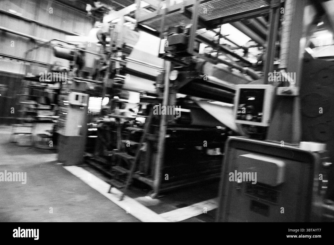 Mr. de Haan Meeuwissen, Whizgle News, Dutch Desk, pays-Bas, 1950 - 2000 on 21-12-1993. L'image montre ces rubriques. La scène présente un vaste cadre industriel, principalement caractérisé par de grandes machines et équipements. Dominant le premier plan est une presse d'impression étendue, présentant une combinaison de surfaces métalliques et de rouleaux de papier vibrants. La machinerie semble usée mais fonctionnelle, avec une toile complexe de tuyaux, d'engrenages et de courroies transporteuses créant un sentiment de complexité. La palette de couleurs est principalement monochrome, avec des nuances de gris, de noir, et des notes de bleu délavé, évoquant Banque D'Images