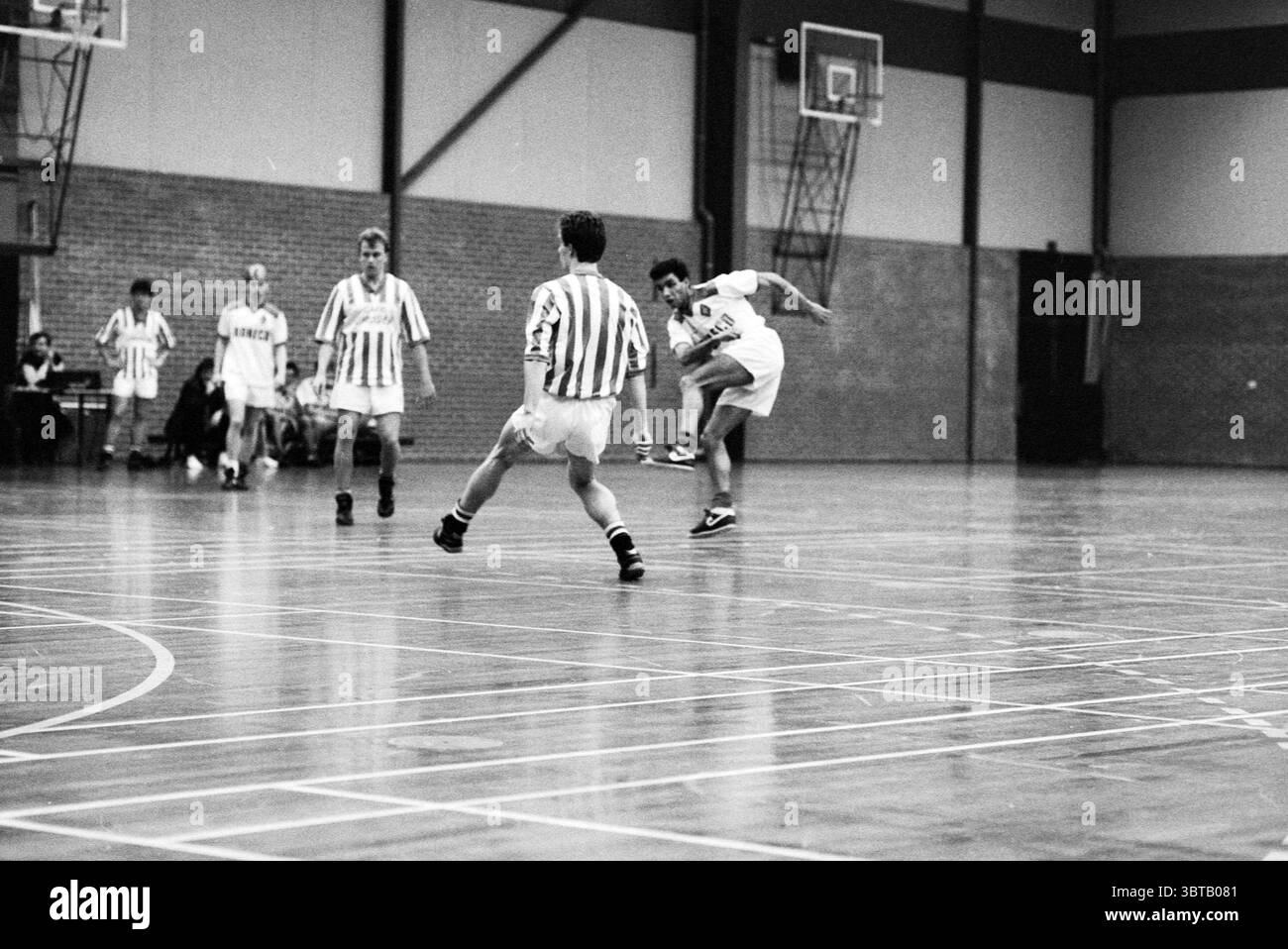 Football en salle Waterloo - Idsten Stormvogels - SVG, Whizgle News, Dutch Desk, pays-Bas, 1950 - 2000 le 11-01-1991. Ces rubriques sont illustrées dans l'image. La scène capture un match de basket-ball en salle dans un gymnase, mettant en vedette un moment dynamique sur le terrain. Au premier plan, deux joueurs sont très engagés. Un athlète porte un uniforme sombre, marqué par un chiffre blanc éclatant, et est en plein air alors qu'il se prépare à tirer sur le basket-ball, affichant un saut impressionnant. Son expression ciblée souligne sa détermination. L'autre joueur, vêtu d'att blanc rayé horizontalement et bleu clair Banque D'Images