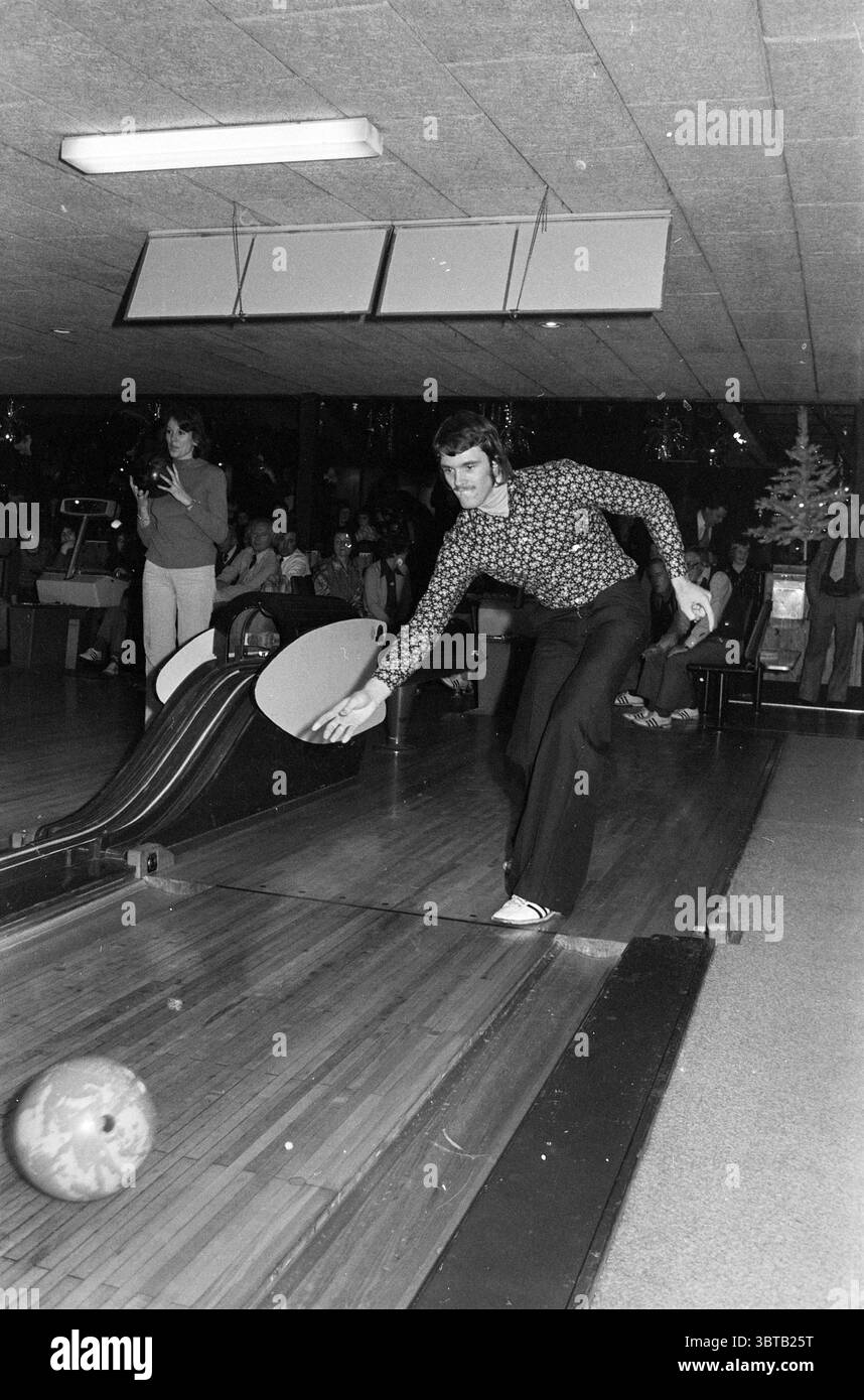 Compétition de bowling., Whizgle News, Dutch Desk, pays-Bas, 1950 - 2000. L'image contient ces rubriques. Dans un cadre de bowling animé, un homme est prêt à l'action, capturé à mi-course avec une attention particulière sur la balle de bowling qui glisse sur la piste. Il porte une chemise en noir et blanc à motifs, son design tourbillonnant offrant un contraste saisissant avec la ruelle en bois lisse sous lui. Son pantalon est sombre, bien ajusté lorsqu'il se penche en avant, incarnant la concentration et la détermination. En arrière-plan, l’atmosphère est remplie d’un mélange d’énergie et d’anticipation. Une petite foule de spectateurs est g Banque D'Images