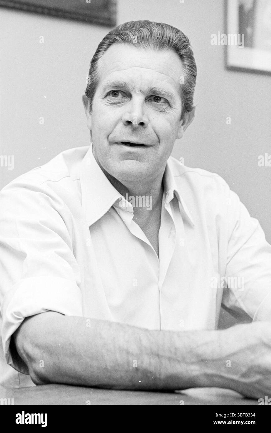 Portrait HR Berk HVB Portraits Football, Whizgle News, Dutch Desk, pays-Bas, 1950 - 2000 le 12-08-1980. Ce sont les éléments de l'image. Un homme d'âge moyen est assis à une table, avec une expression réfléchie sur son visage. Ses cheveux sont coiffés soigneusement, avec des traces de gris qui suggèrent la maturité. Il porte une chemise à manches courtes de couleur claire qui semble nette et nette, accentuant la simplicité de son look général. Le cadre a une couleur de mur neutre et discrète qui met l'accent sur l'homme. L'éclairage est doux, projetant des ombres douces qui mettent en valeur ses traits sans être dur. T Banque D'Images