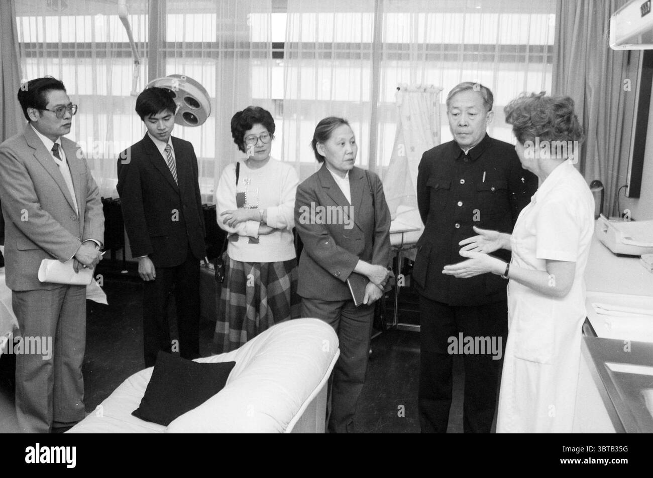 Visite du ministre chinois de la planification familiale aux hôpitaux de la ce Haarlem Boerhaavelaan pays-Bas, Whizgle News, Dutch Desk, pays-Bas, 1950 - 2000 le 18-02-1987. L'image contient ces rubriques. La scène se déroule dans un environnement médical ou clinique, caractérisé par des lignes propres et stériles et une atmosphère lumineuse. L'éclairage est doux et diffus, filtrant à travers des rideaux blancs transparents qui adoucissent l'apparence générale de la pièce. Au centre, un groupe d'individus est engagé dans la conversation, leurs expressions reflétant la curiosité et l'attention. Ces chiffres incluent les deux hommes A. Banque D'Images