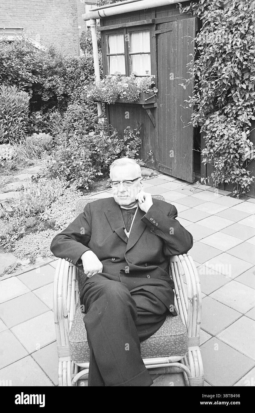 Pastor Taaman Persons, Whizgle News, Dutch Desk, pays-Bas, 1950 - 2000 le 13-07-1965. Voici les rubriques de l'image. La scène capture un cadre de jardin calme, avec une figure importante assise dans une chaise en osier. L'individu, vêtu d'un costume sombre, s'assoit avec une expression réfléchie, une main reposant sur son menton. Ses lunettes reflètent une lumière douce, ajoutant un point fort subtil à son comportement contemplatif. Autour de lui, un jardin luxuriant regorge de verdure, avec diverses plantes et fleurs qui apportent des éclaboussures de couleur au milieu des tons majoritairement monochromes du cadre. T Banque D'Images
