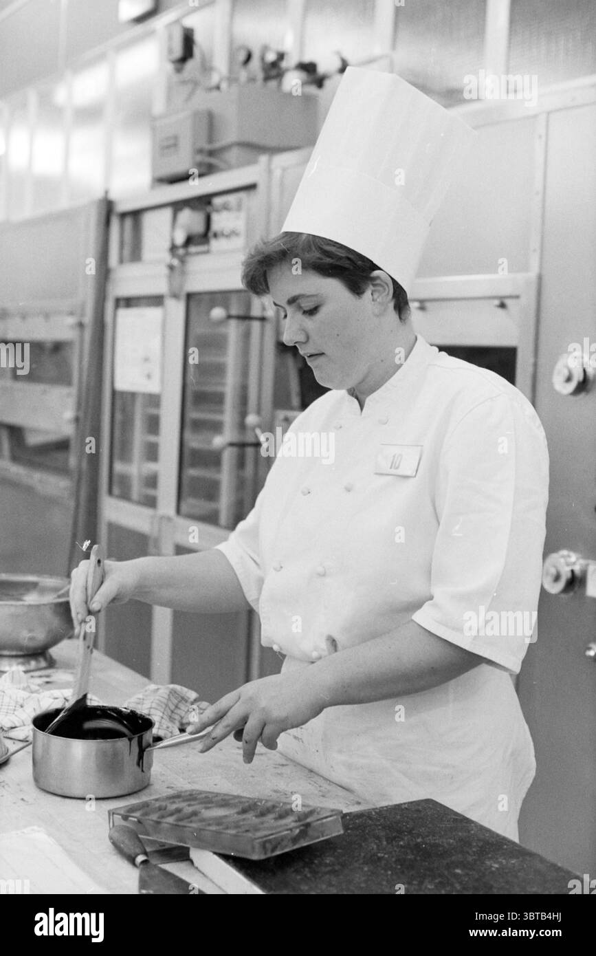 Pâtisserie Bakers SG Haarlem Haarlem pays-Bas, Whizgle News, Dutch Desk, pays-Bas, 1950 - 2000 le 05-10-1992. L'image contient ces rubriques. La scène met en scène un artiste culinaire concentré dans un cadre de cuisine. La personne est vêtue d'un manteau de chef blanc traditionnel, avec un haut chapeau de chef plissé blanc qui ajoute une touche professionnelle. Leur expression transmet la concentration comme ils remuent un pot sur un poêle, mettant en valeur le sérieux de leur métier. Le comptoir est encombré d'outils culinaires, y compris un bol à mélanger, des ustensiles et une plaque de cuisson, indiquant un Cooki actif Banque D'Images