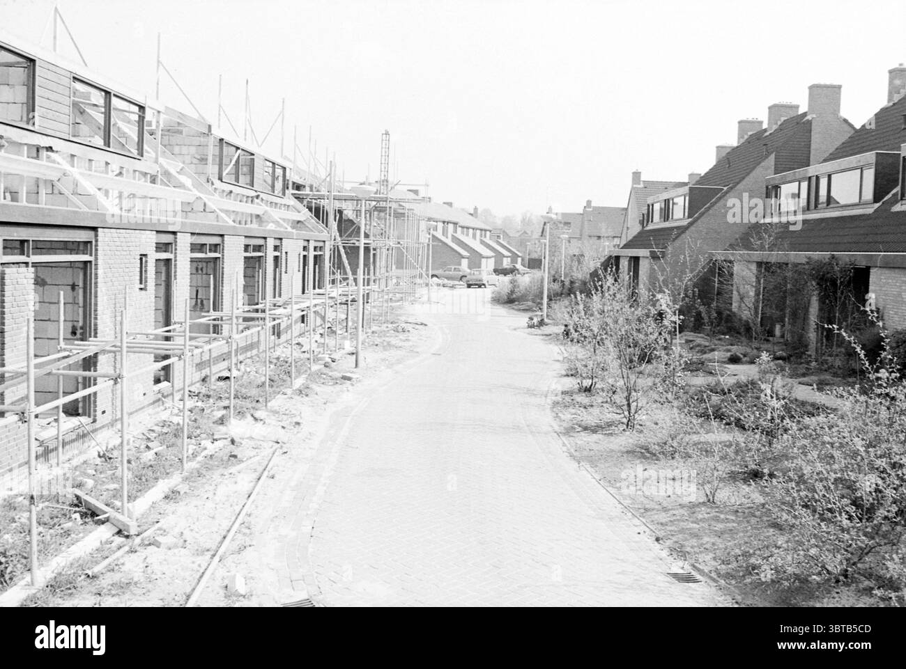 Maisons neuves de Hulstlaan B'broek Nouvelle construction Bennebroek Van der Hulstlaan, Whizgle News, Dutch Desk, pays-Bas, 1950 - 2000 on 07-05-1979. L'image montre ces rubriques. La scène capture un quartier calme au milieu du développement. D’un côté, plusieurs maisons sont en construction, caractérisées par des cadres apparents et des échafaudages qui laissent entrevoir les travaux en cours. Les maisons, en brique, ont une texture rustique qui contraste avec le raffinement de l'échafaudage métallique. Le trottoir courbe le long de la rue, donnant à la zone une sensation de flux et de mouvement. Environnant th Banque D'Images