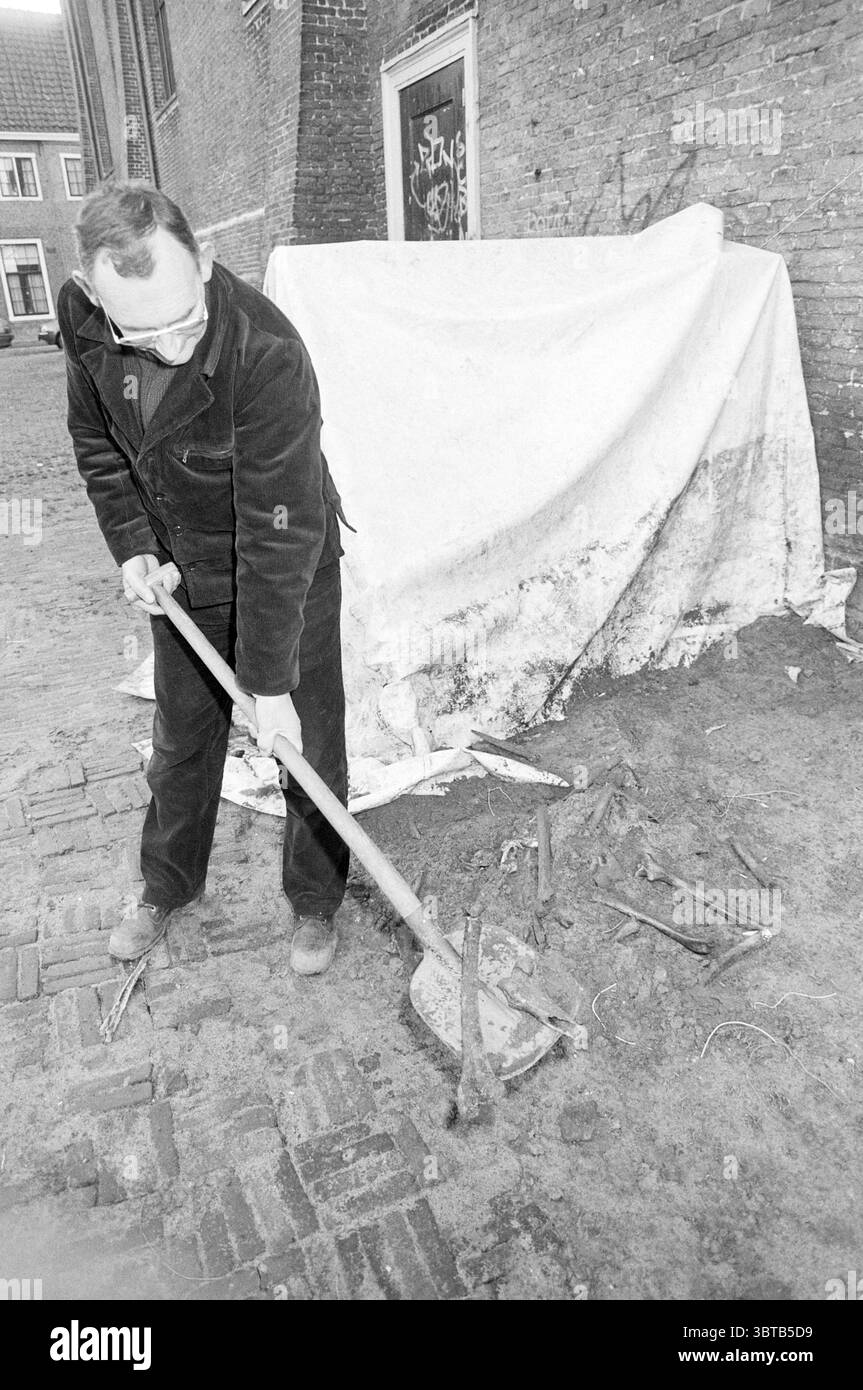 Creuser des os Nieuwe Kerksplein fouilles Haarlem Nieuwe Kerksplein pays-Bas, Whizgle News, Dutch Desk, pays-Bas, 1950 - 2000 on 18-01-1989. Ce sont les éléments de l'image. Dans la scène, un homme est positionné dans un cadre quelque peu extérieur, s'engageant dans une activité qui transmet un sentiment de travail manuel. Il est vêtu de vêtements sombres et décontractés qui contrastent avec les tons plus légers et plus discrets de l'environnement. Le sol sous lui est composé de pavés, créant une surface texturée qui ajoute de la profondeur à la composition. Devant lui, il tient un outil à long manche, l Banque D'Images