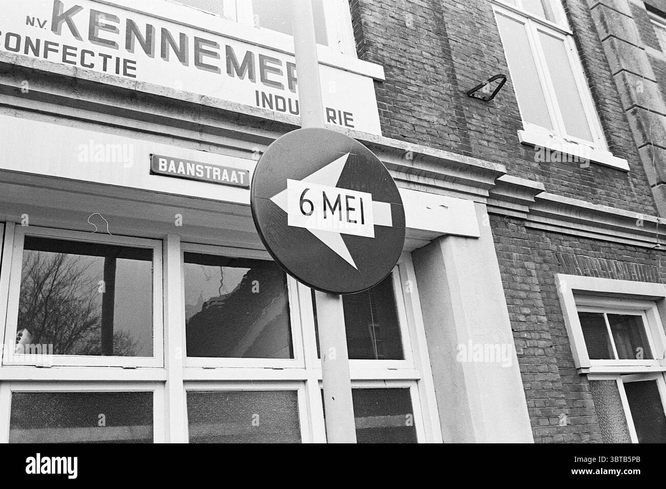 Panneaux routiers avec date Haarlem Baanstraat pays-Bas, Whizgle News, Dutch Desk, pays-Bas, 1950 - 2000 le 24-04-1969. L'image inclut ces rubriques. La scène représente un cadre urbain classique caractérisé par un mélange d'éléments architecturaux. Un grand bâtiment en briques occupe la toile de fond, mettant en valeur un style industriel vintage avec plusieurs fenêtres encadrées en blanc. Ces fenêtres sont divisées en vitres plus petites, permettant un aperçu de l'intérieur, qui semble bien éclairé. Un signe proéminent est suspendu à un poteau au premier plan, de forme circulaire avec une bordure noire. Dans le cercle, a Banque D'Images