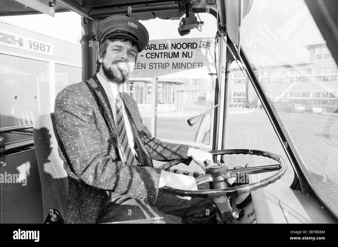 Alderman Koster à NZH en relation avec les nouveaux conseillers de zonage, Whizgle News, Dutch Desk, pays-Bas, 1950 - 2000 le 30-01-1987. Ces rubriques apparaissent dans l'image. La scène met en scène un chauffeur de bus assis dans le poste de conduite d'un bus, affichant un comportement confiant et amical. Il a une barbe complète et est habillé dans un uniforme classique qui comprend une veste de couleur foncée et une cravate rayée avec des nuances claires et sombres, suggérant une apparence professionnelle. L'intérieur du bus est caractérisé par un design propre et fonctionnel. Le siège du conducteur est placé à l'avant, ce qui permet Banque D'Images