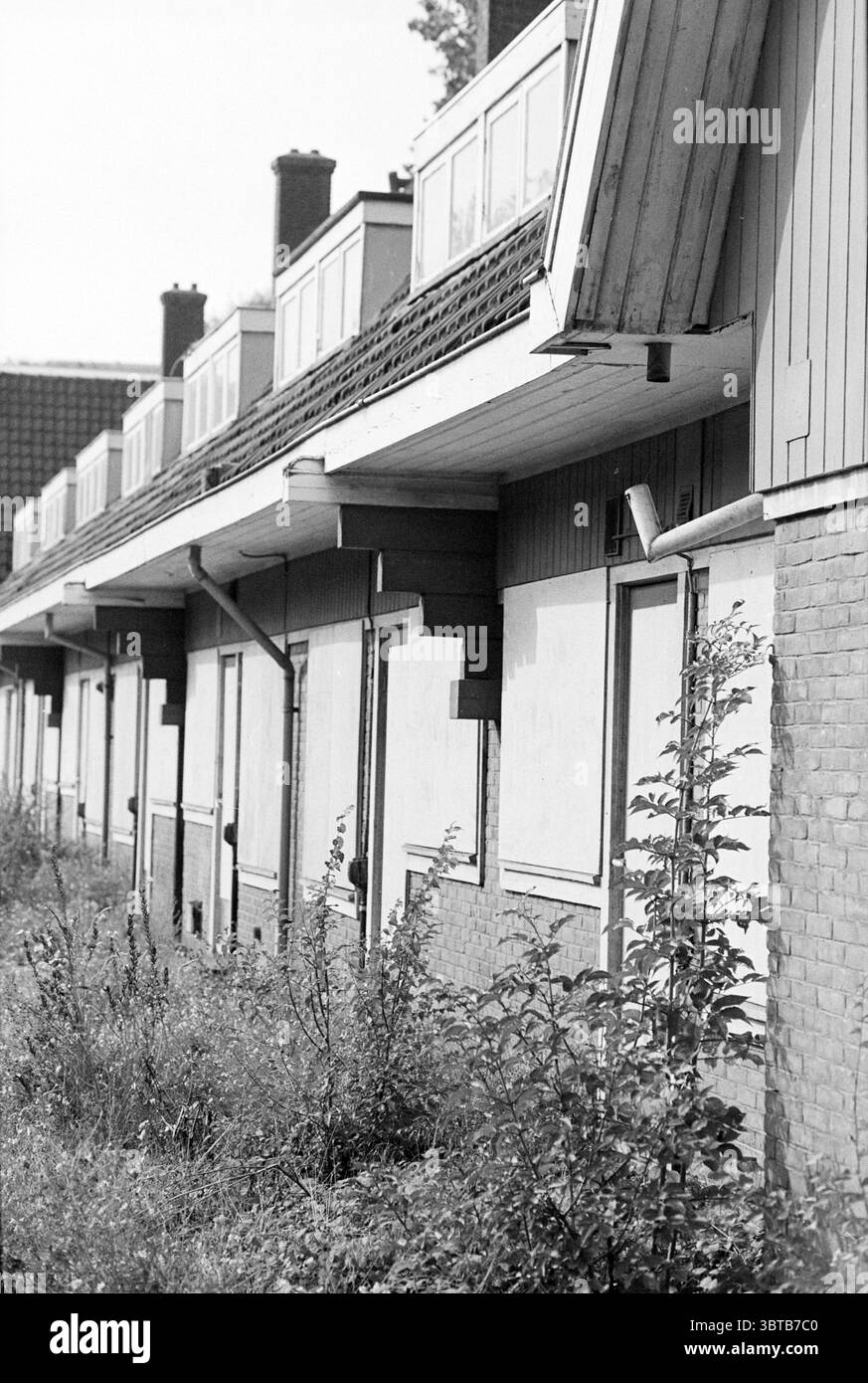Rangée de Boarded Up Houses Hoogovens, Whizgle News, Dutch Desk, pays-Bas, 1950 - 2000 on 11-09-1995. L'image inclut ces rubriques. La scène représente une rangée de bâtiments altérés, caractérisés par un aspect quelque peu négligé. L'architecture présente une combinaison de briques et d'éléments en bois, avec un toit en pente qui fait saillie à des angles impairs, suggérant une usure au fil du temps. Les murs sont principalement d'une couleur sourde, avec un peu de décoloration et de décollement de la peinture, contribuant à un sentiment général d'abandon. Les fenêtres sont embarquées, leurs couvertures ajoutant à l'obscurité du décor. Surroundin Banque D'Images