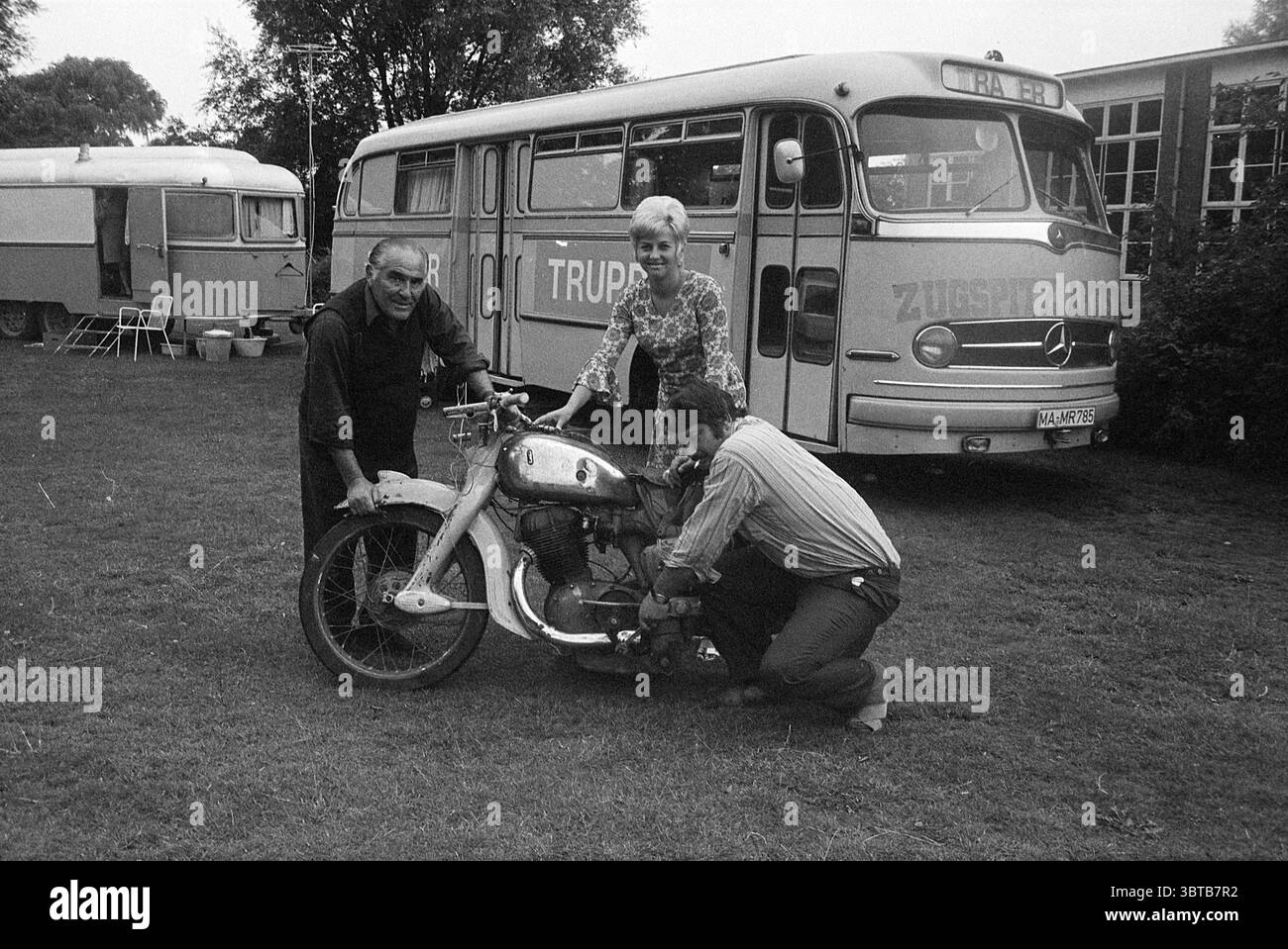Acrobats Beverwijk Circus, Whizgle News, Dutch Desk, pays-Bas, 1950 - 2000 le 05-08-1971. Ce sont les éléments de l'image. La scène se déroule dans une zone herbeuse, où l'herbe verte éclatante s'étend au premier plan, contrastant subtilement avec les tons discrets des véhicules et personnages environnants. En arrière-plan, un grand bus au design vintage domine la scène, présentant un corps de couleur claire avec un motif textural distinct et des bords courbes, indiquant son époque classique. Le bus est garé à côté d'un autre véhicule de style caravane, les deux ajoutant à l'ambiance nostalgique des s. Banque D'Images