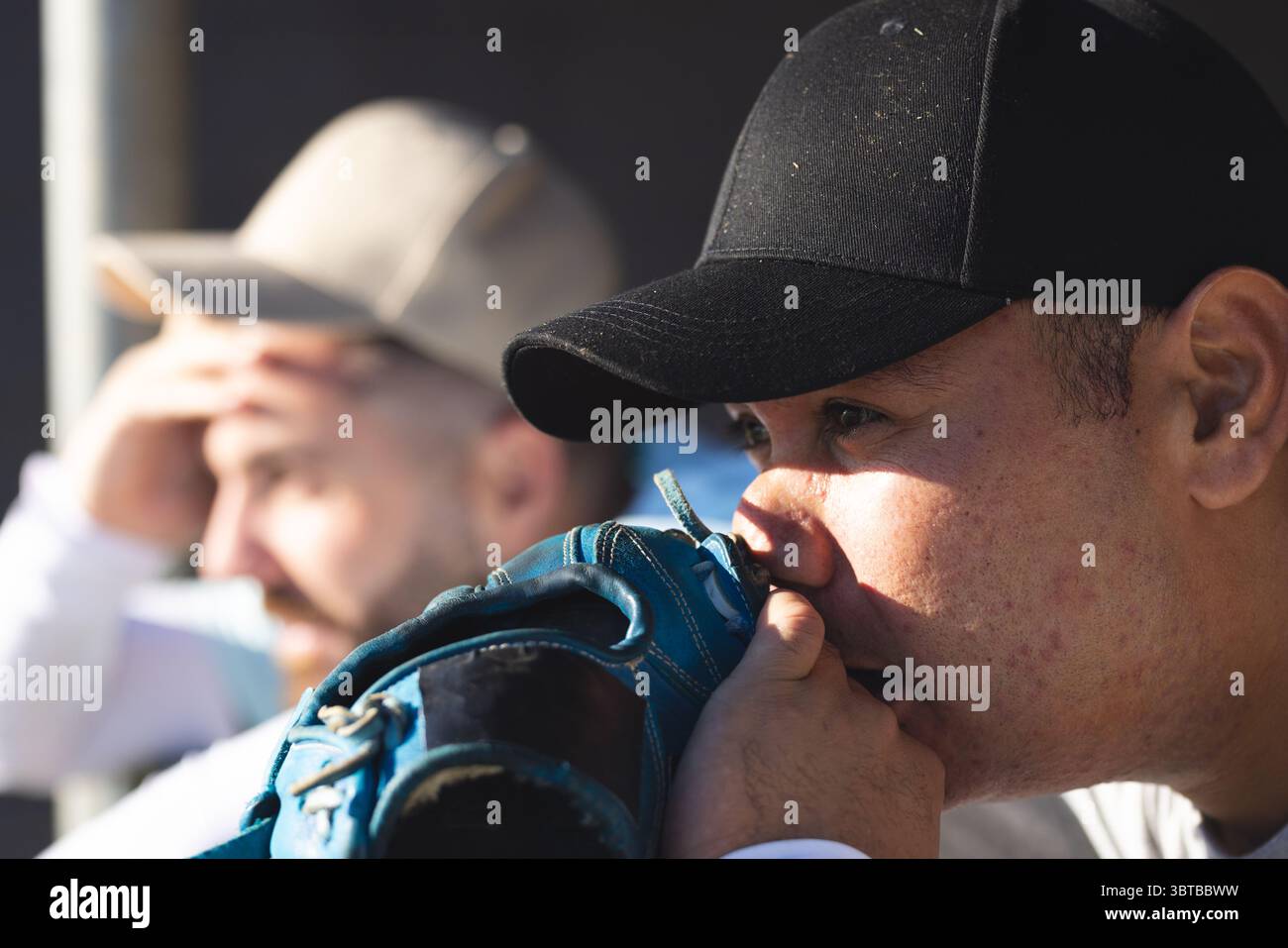 Divers coéquipiers masculins portant des casquettes de baseball assis sur un banc de dugout, tenant des gants bleus protégeant les yeux Banque D'Images