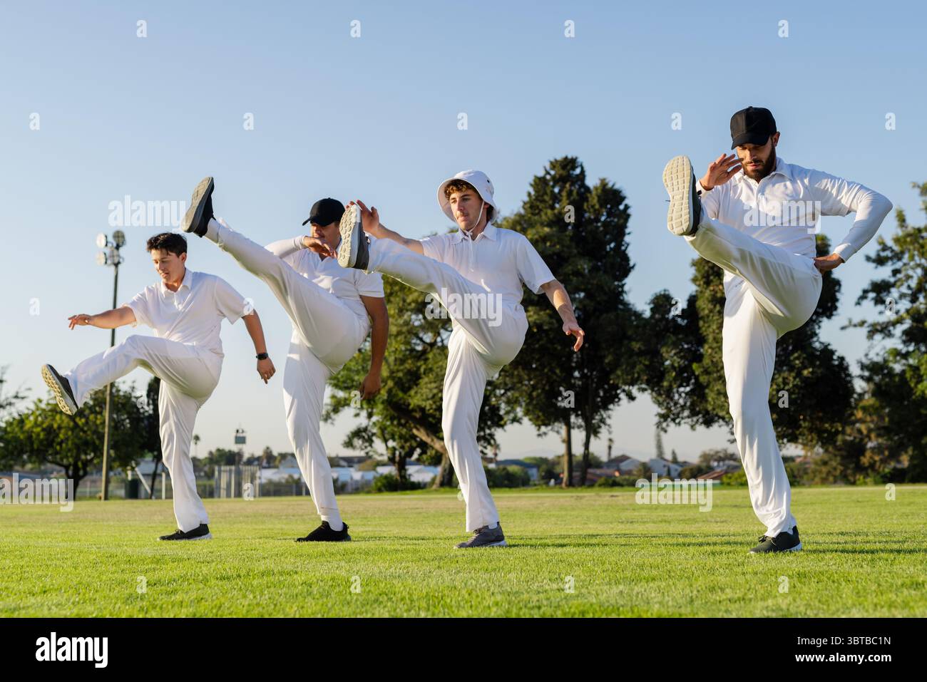 Divers coéquipiers masculins se tenant haut sur un terrain herbeux portant des uniformes blancs et un chapeau seau Banque D'Images