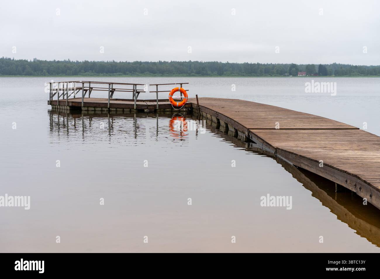 Vue calme sur le front de mer avec quai et bouée de sauvetage sur un lac immobile, reflétant le ciel d'été - concept de tranquillité et de sécurité. Banque D'Images