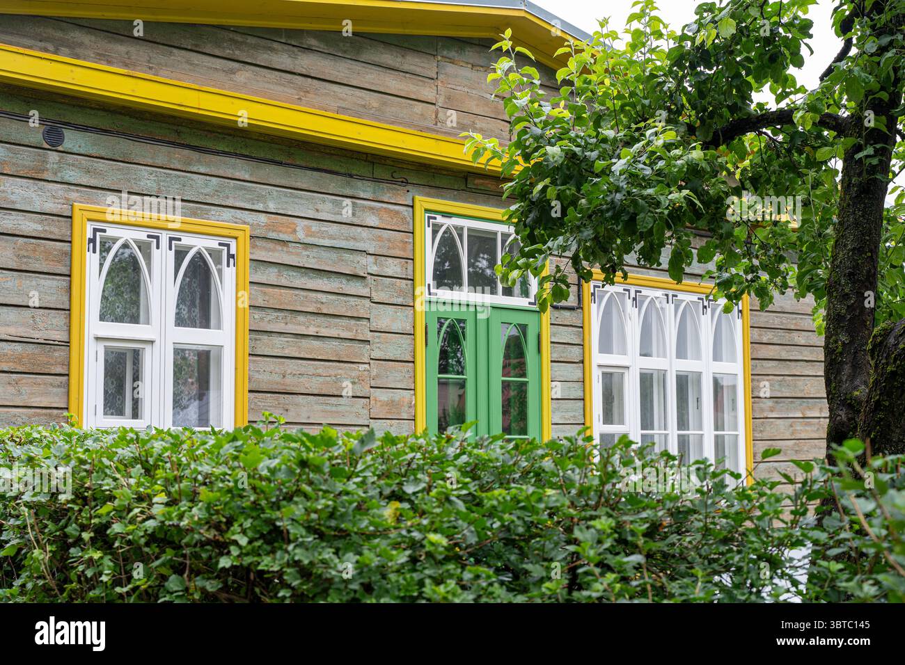 Maison traditionnelle en bois avec garniture jaune et porte verte à Võru, Estonie - charme architectural rural sur une journée nuageuse d'été. Banque D'Images