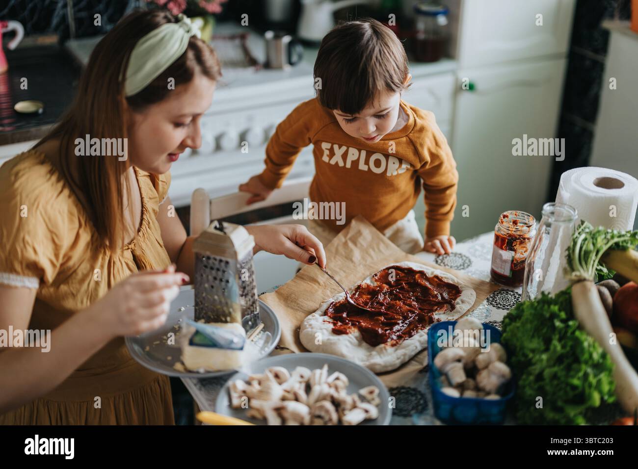 Mère et enfant faisant une pizza maison ensemble dans une cuisine confortable Banque D'Images
