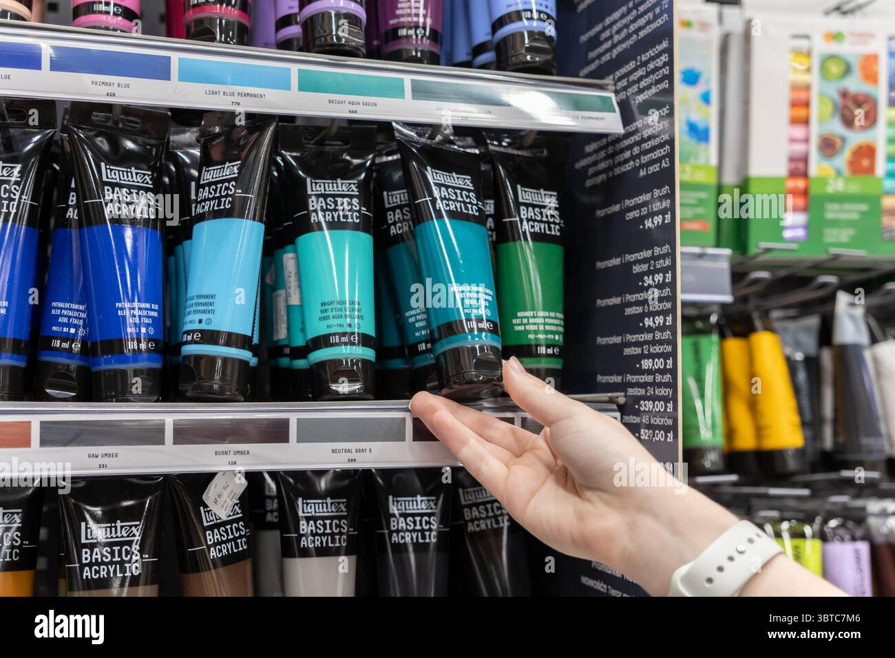 Poznan, Pologne - 30 juin 2025 : une main sélectionne les tubes de peinture acrylique Liquitex Basics dans une étagère de magasin, illustrant les achats de rentrée scolaire pour essent Banque D'Images